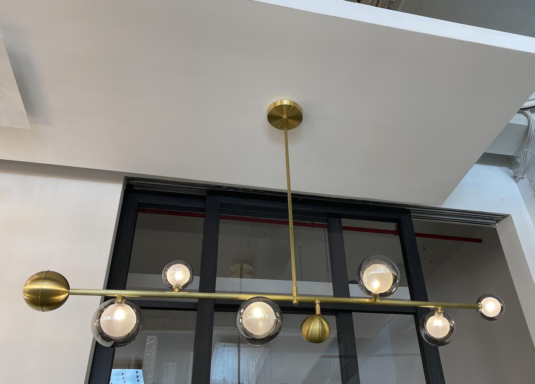A chandelier consisting of a horizontal metal rod attached to the ceiling by a vertical rod in the middle and of Kadur glass pendants and metal orbs on the horizontal rod which provide multiple sources of light. The central metal orb contains an