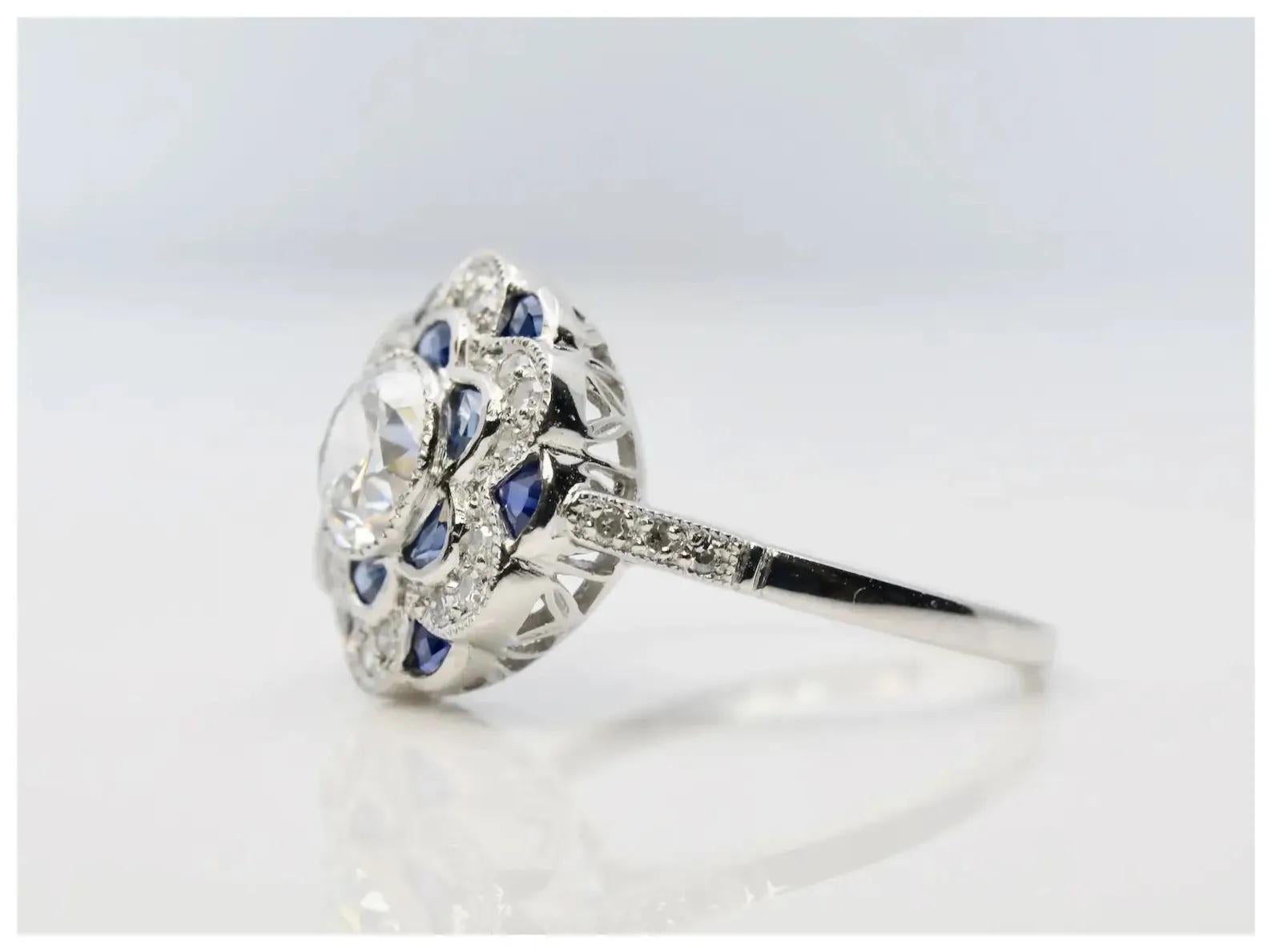 An Art Deco style diamond, and sapphire ring in platinum.

Centered by a 0.81 carat H color, SI1 clarity old European cut diamond set in a milligrained platinum bezel.

Framing the center diamond are 12 bespoke French cut sapphire petals, and 24