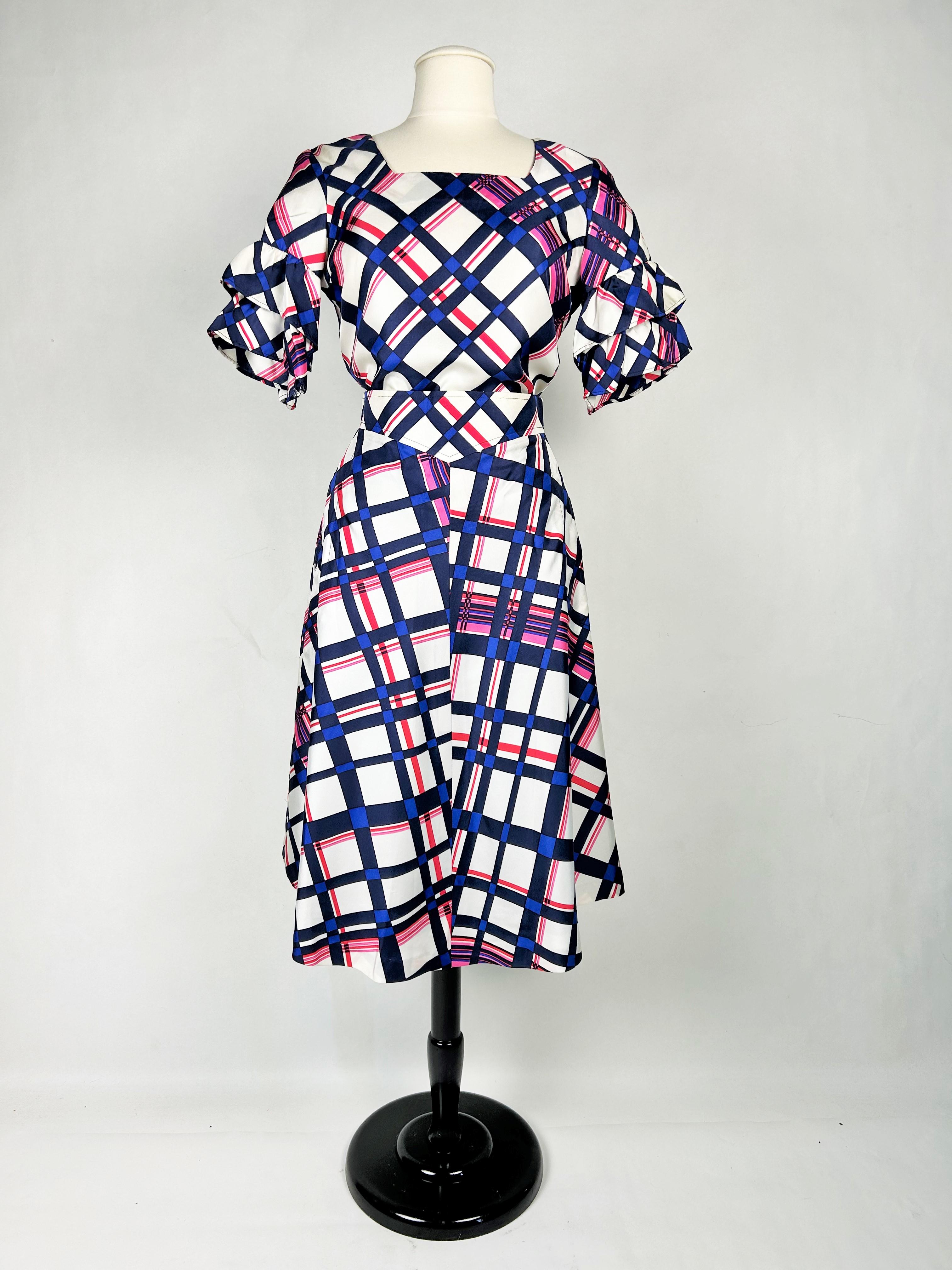 Circa 1972
Francia
Completo da cocktail estivo con camicetta e gonna, disegnato da Pierre Cardin Paris e risalente ai primi anni Settanta. Twill di seta di qualità finissima lavorato in sbieco a quadri bicolore in blu navy e rosa. Top blusa, taglio