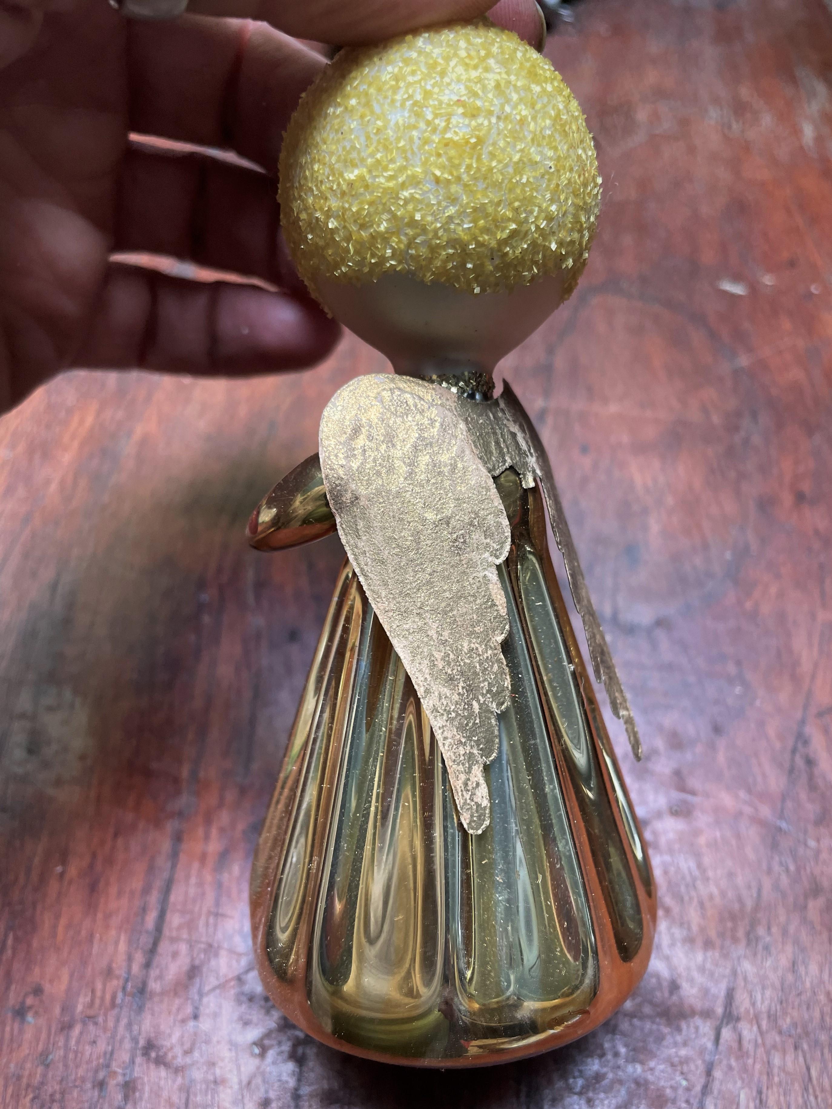What an incredibly cute angel caroler Christmas ornament made from blown glass with textured yellow pieces glued to the head for hair and gold textured pieces glued down the front and around the neck as a choker. The wings are heavy paper coated