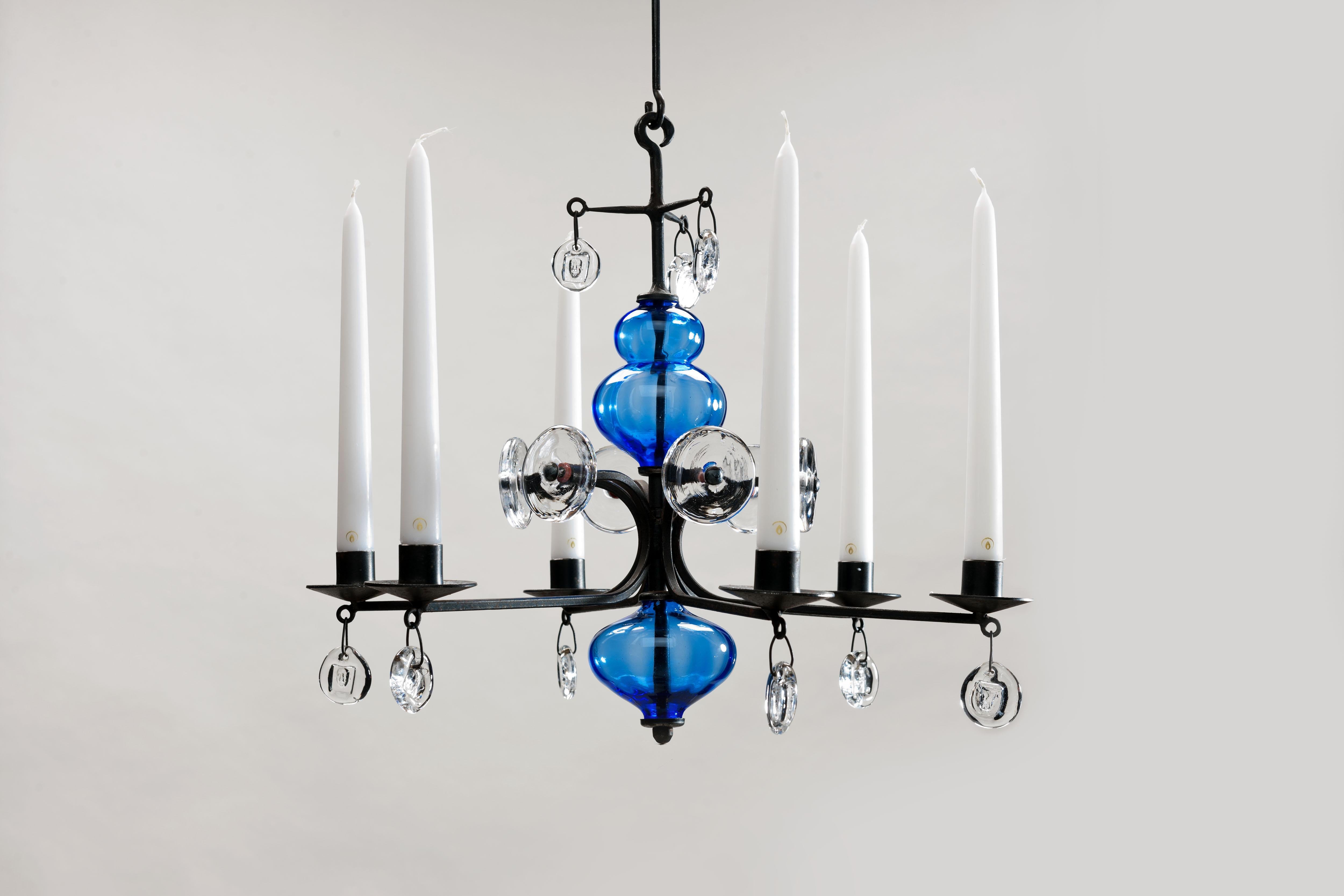 Kronleuchter für 6 Kerzen des schwedischen Designers Erik Hoglund aus geschwärztem Eisen mit blauen Glasornamenten und verschiedenen handgefertigten Glasscheiben mit eingeprägten Bildern von verschiedenen Gesichtern. 
Der Kronleuchter wird mit zwei