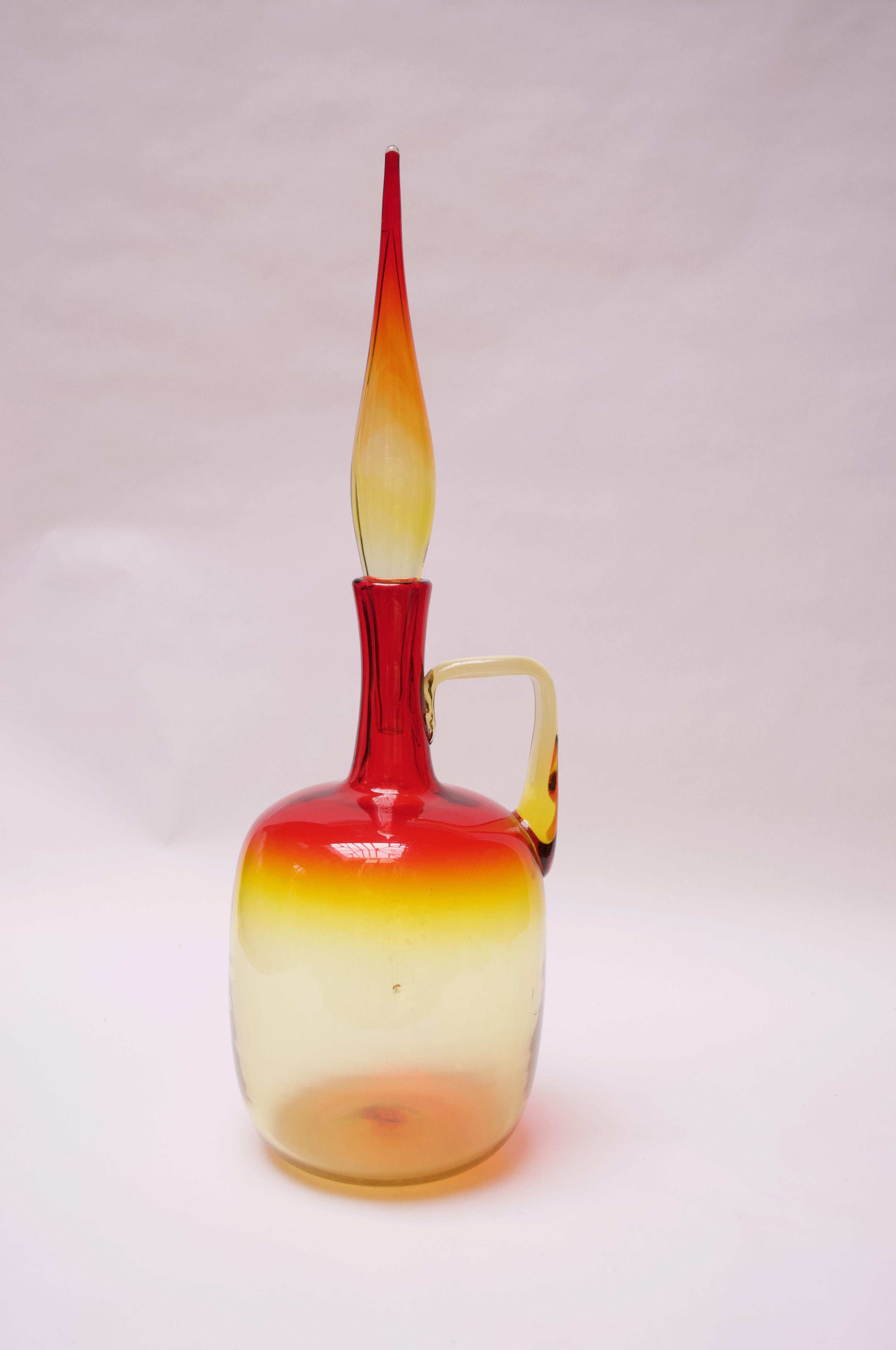 Blown glass decanter designed in the 1960s by Wayne Husted for Blenko. Uncommon example with applied handle and original flame stopper. Large size and attractive amberina / tangerine palette in bold red and yellow. 
Features Blenko's signature