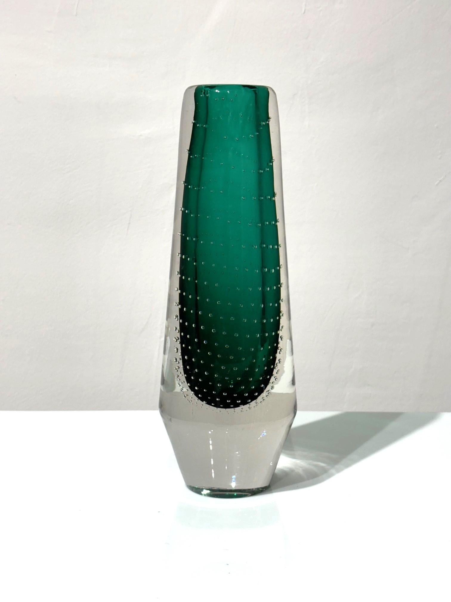 This 1960s vase is made of a thick clear glass decorated with bubbles and a layer of dark green tinted glass on the inside. 
The thickness of the glass, the reflection of light on the bubbles, the intensity of the color make it a particularly