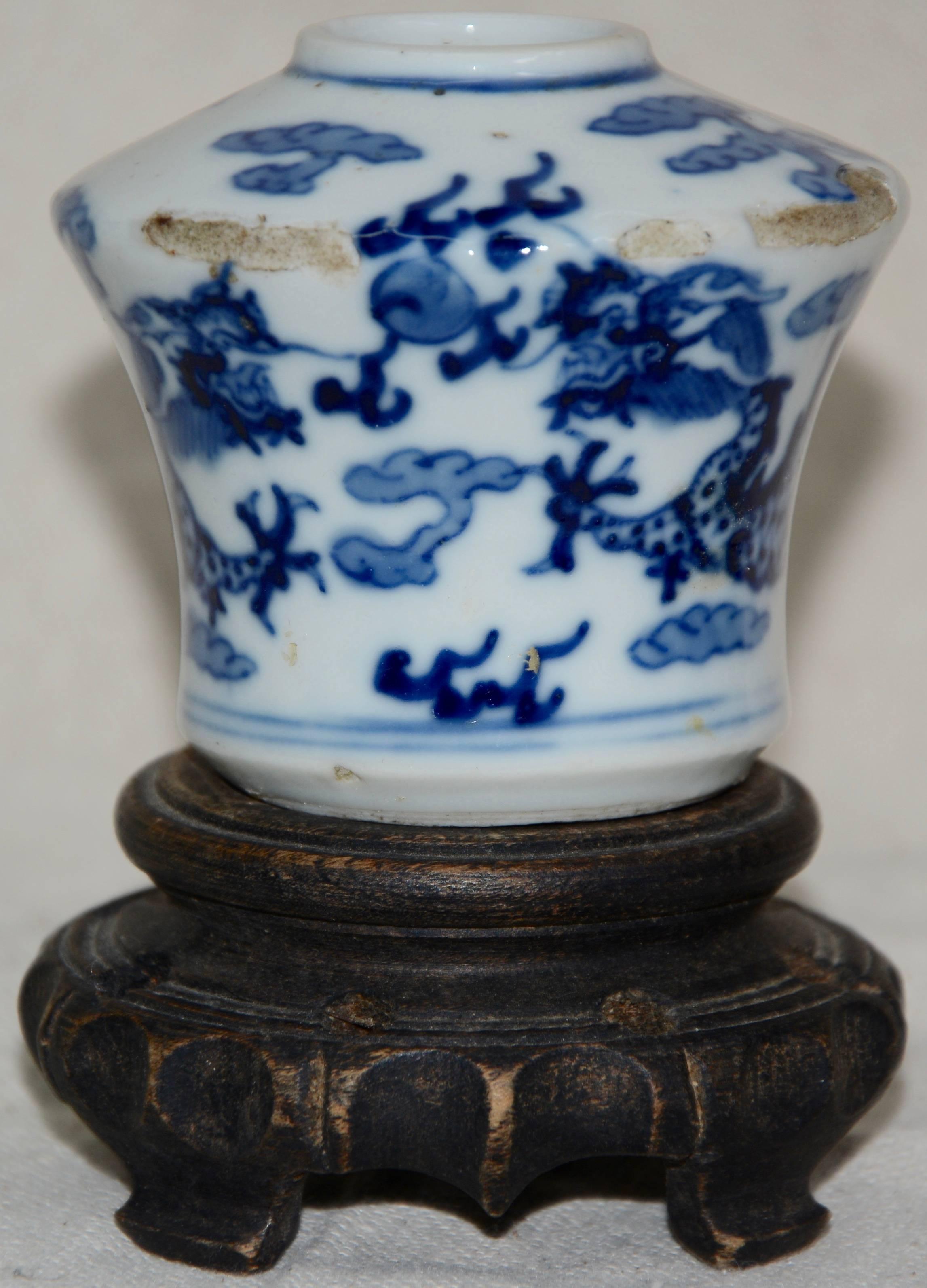 Blue hand painted details accent this unique white Asian ceramic vessel. It is marked on the bottom of the piece. The unusual shape of the ceramic sits atop a hand carved wooden base to enhance its beauty.