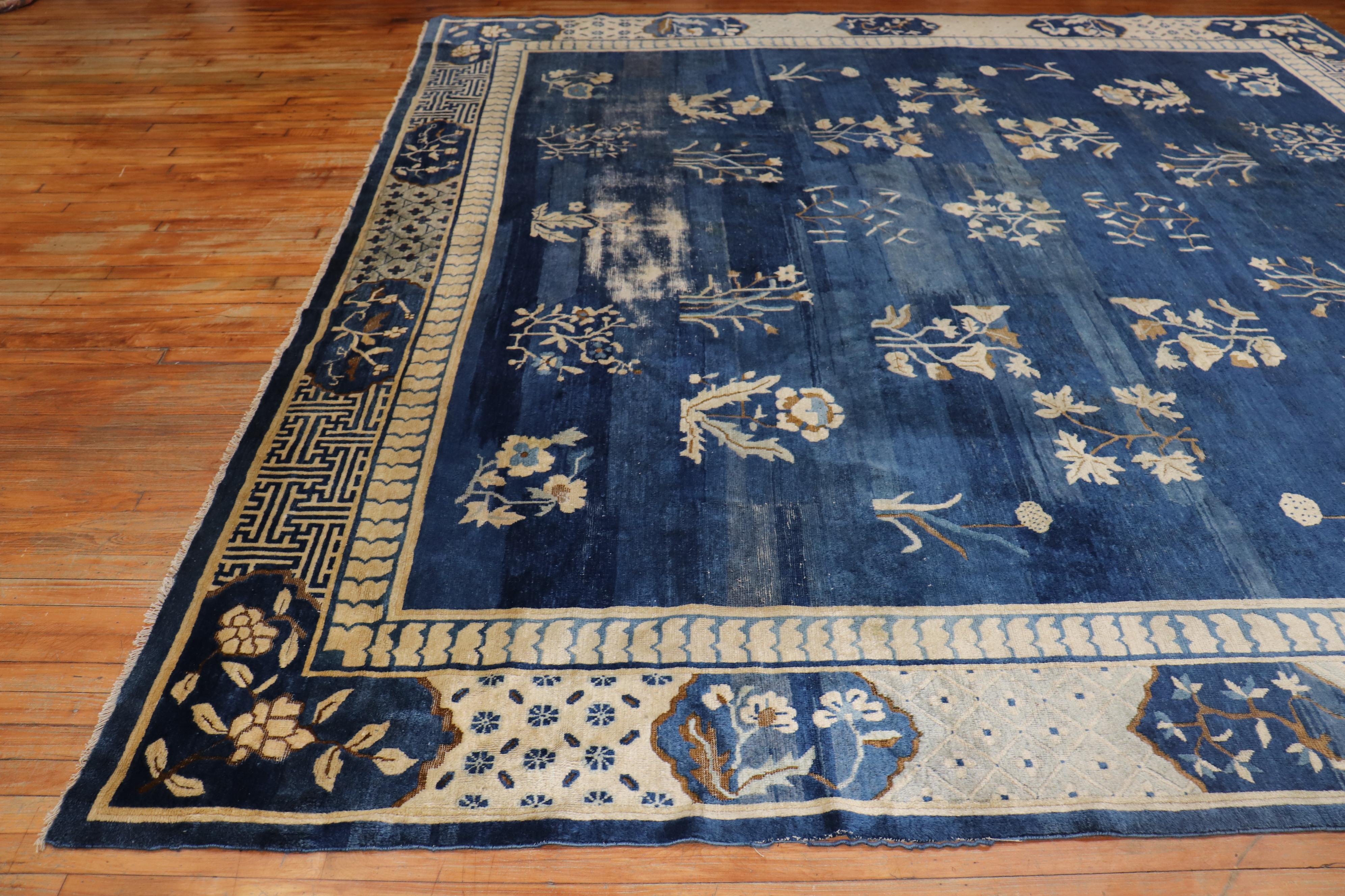A rare 11-foot square early 20th-century shabby chic weather textured Chinese rug with a graphic floral Motif in denim blue, accents in white, and hints of brown

Measures: 11' x 11'1