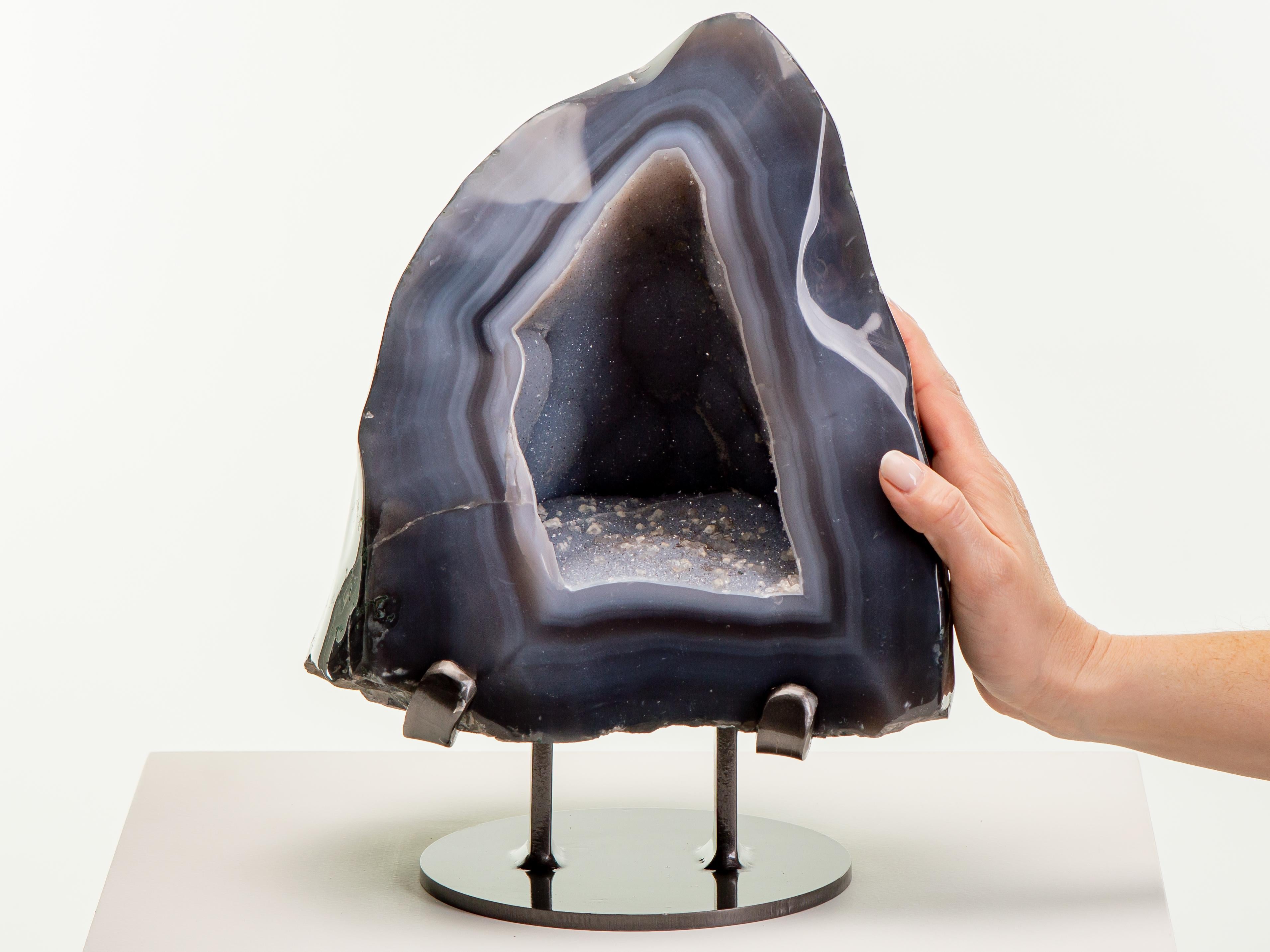 Une belle formation pyramidale avec une épaisse bordure d'agate à bandes bleues.
La cavité centrale ressemble à une grotte avec un plancher de quartz druzeux et de calcite.
cristaux. Des stalactites naissantes ornent la paroi arrière.

Cette