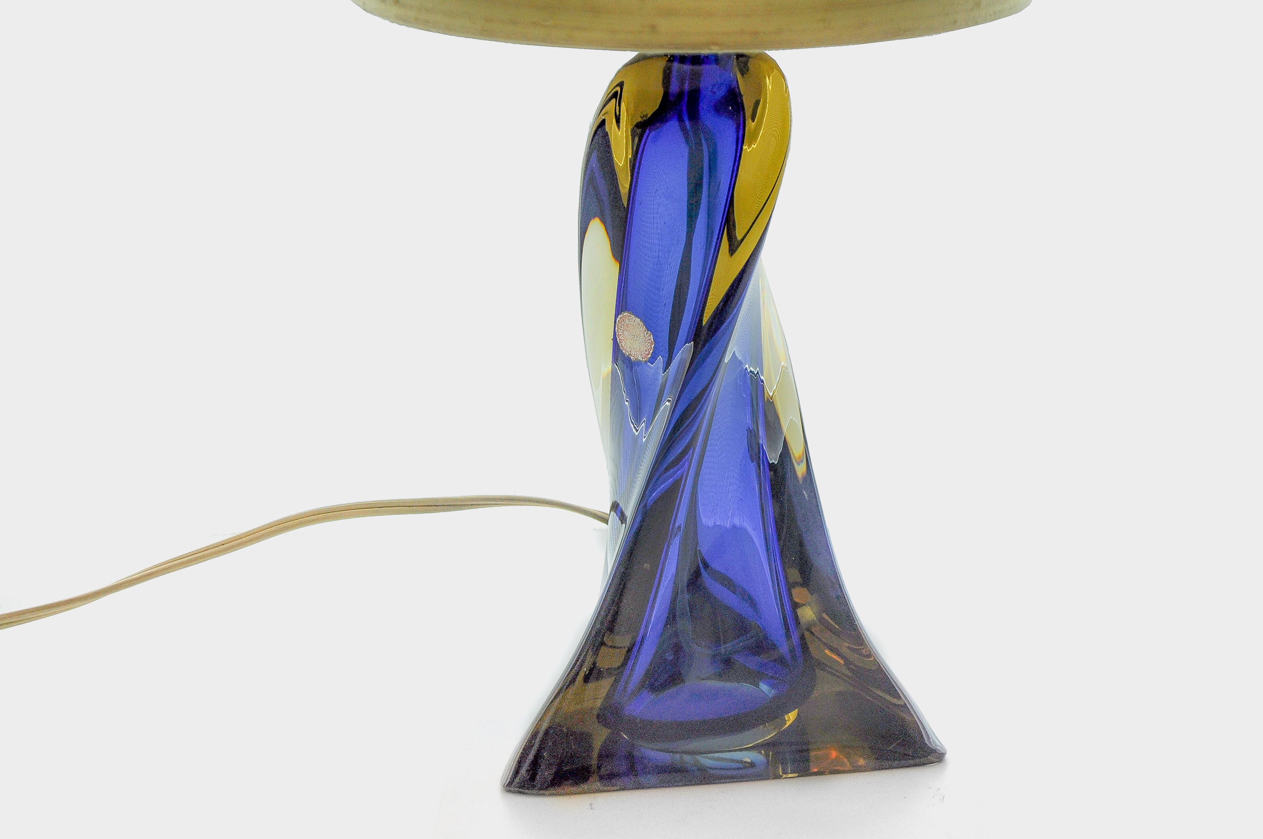 This small table lamp made of two-colored Murano glass comes from the glass factory of Archimede Seguso. It is a blue/amber colored glass with a triangular base, which is tapered in a spiral shape. The original shade is beige with a subtle