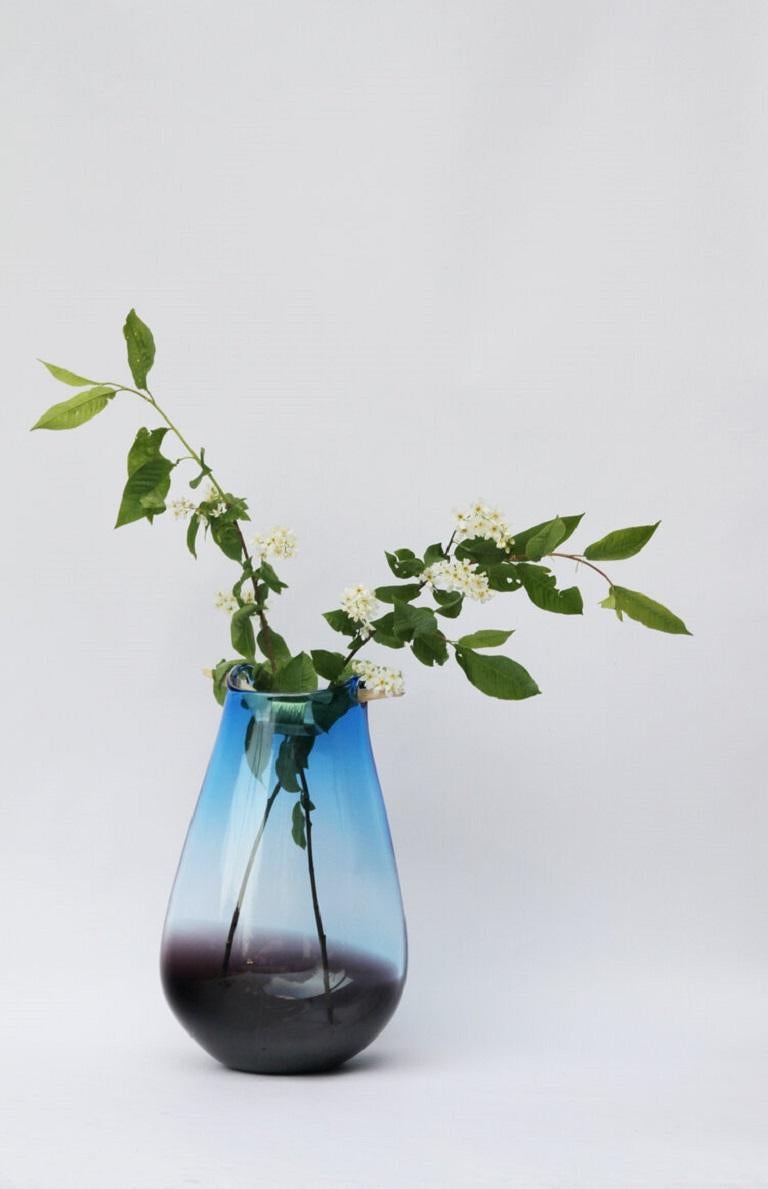 Blue and brown Heiki vase, Pia Wüstenberg
Dimensions: D 20-22 x H 32-40
Materials: glass, wood, metal wire
Available in other colors.

Inspired by a simple fix on an old sauna ladle handle, fixed with wire and outright everyday genius. Heiki