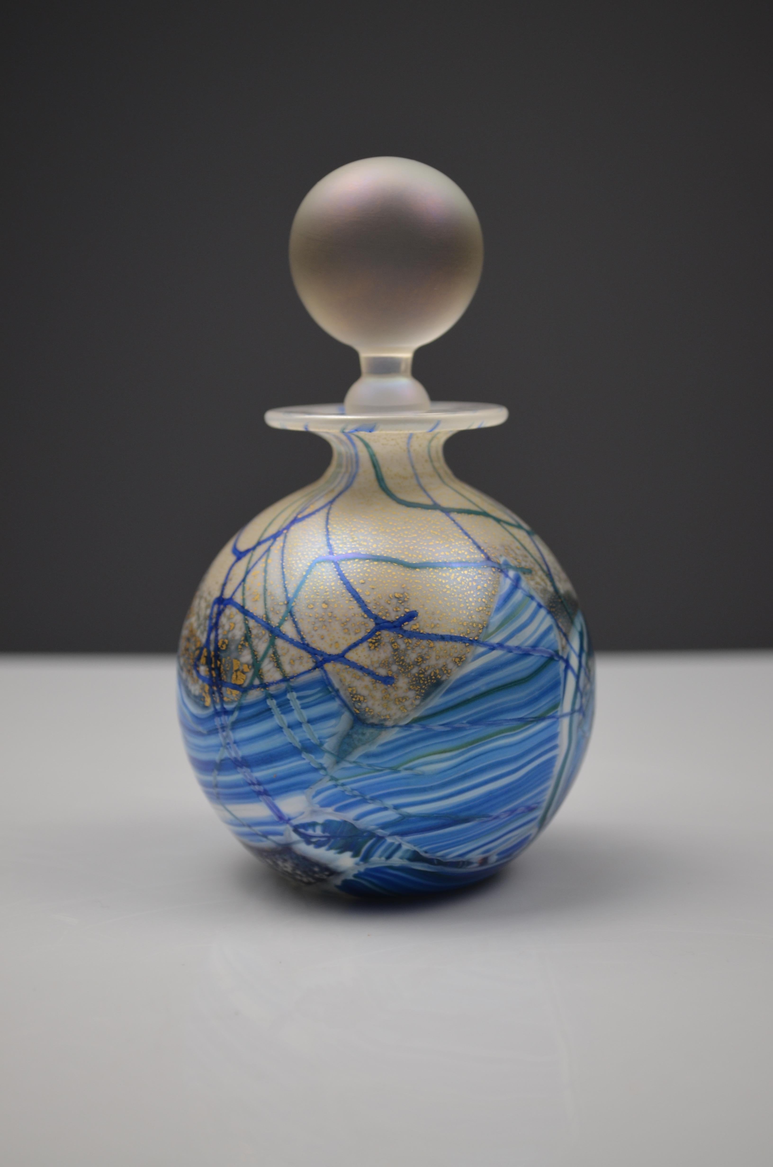 Atemberaubender Parfümflakon aus mundgeblasenem Glas von dem renommierten Isle of Wight Studio Glass.
Dieses Stück zeichnet sich durch eine reiche Verzierung mit goldenen Blattakzenten, fließenden blauen Bahnen und wirbelndem mehrfarbigem Glas in