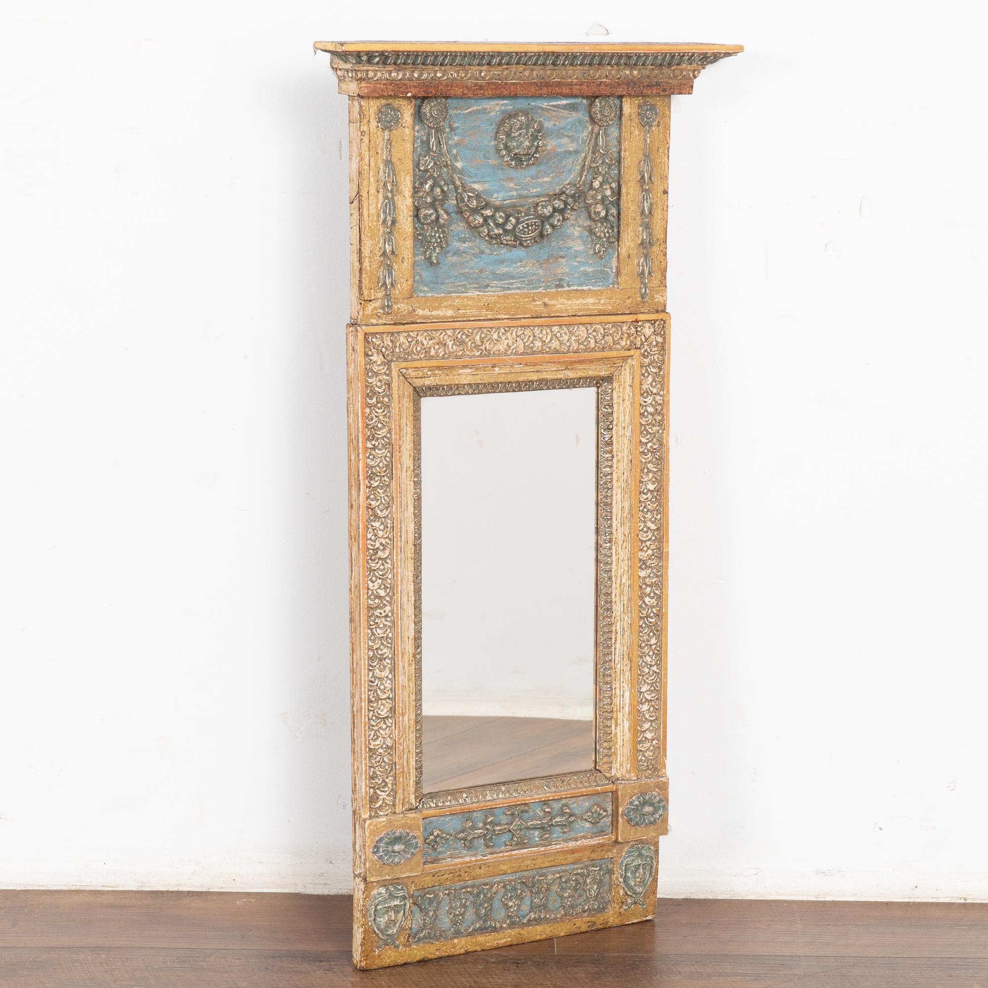 Lovely Swedish trumeau mirror with upper section decorated with applied carved swag of fruits and lion's head against soft blue background.
Beautiful shades of gold, bronze, blue, muted red and touches of teal are seen throughout accenting the