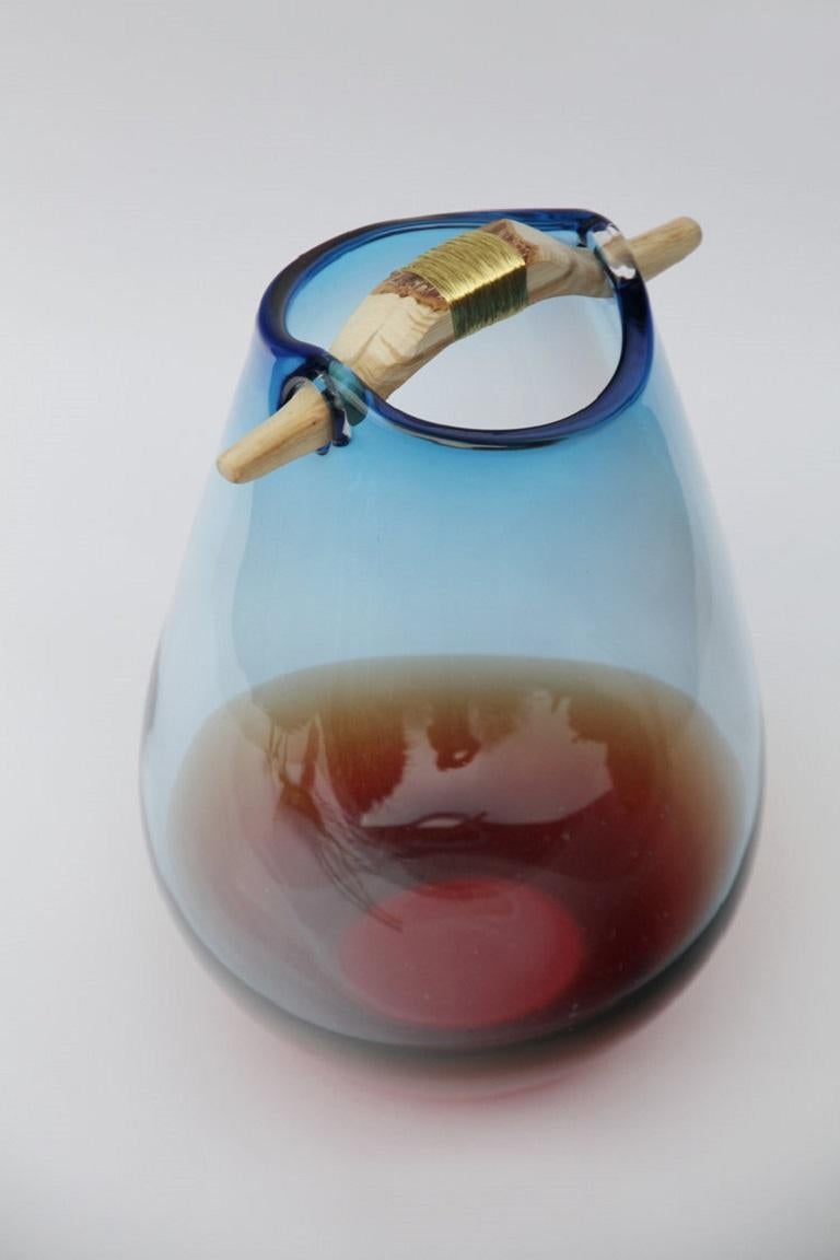 Vase Heiki bleu et orange III, Pia Wüstenberg
Dimensions : D 20-22 x H 32-40
MATERIALES : verre, bois, fil métallique.
Disponible dans d'autres couleurs.

Inspiré d'une simple réparation d'un vieux manche de louche de sauna, fixé avec du fil de fer