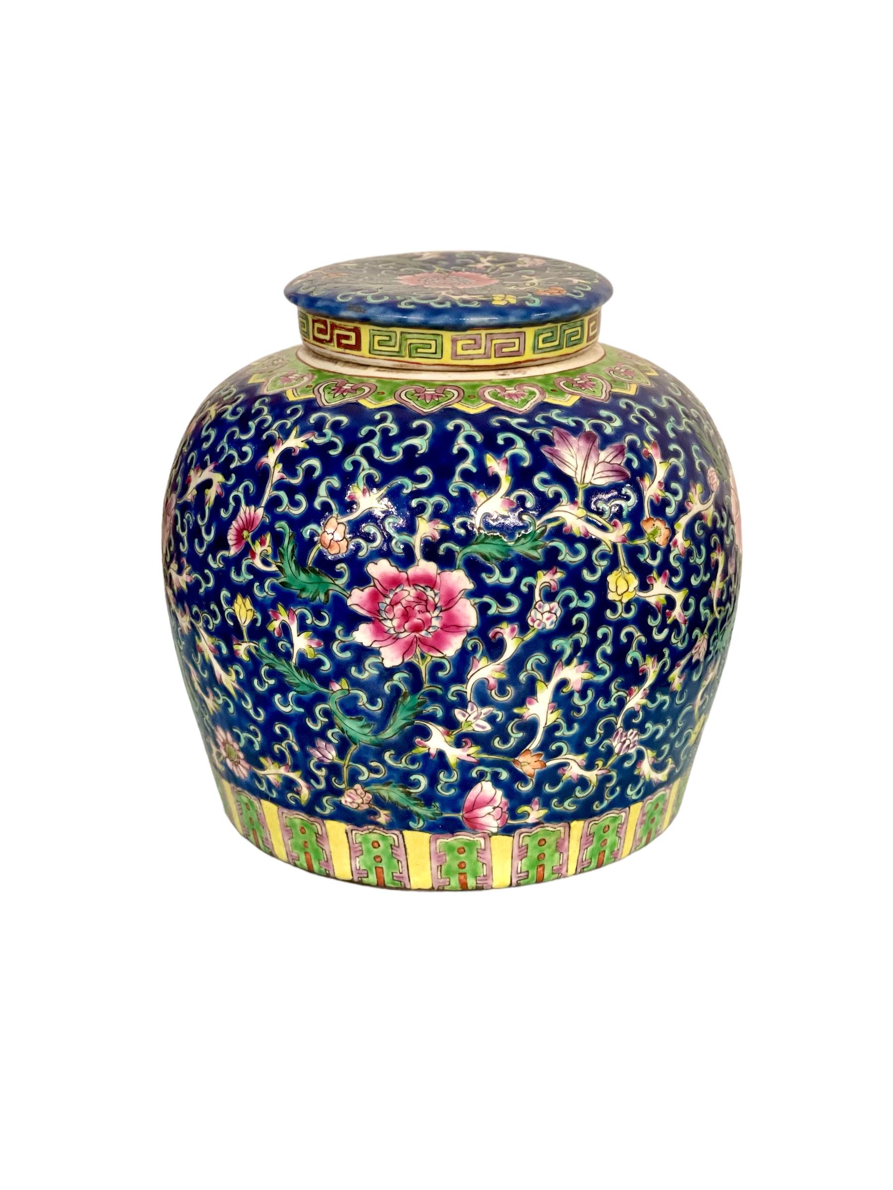 A large and very striking hand-painted lidded pot in Straits porcelain, featuring a vibrant cobalt-blue background with profusely detailed enamelled foliage and 'Famille Rose' (or Fencai) motifs in a colourful palette. The base features a stylised