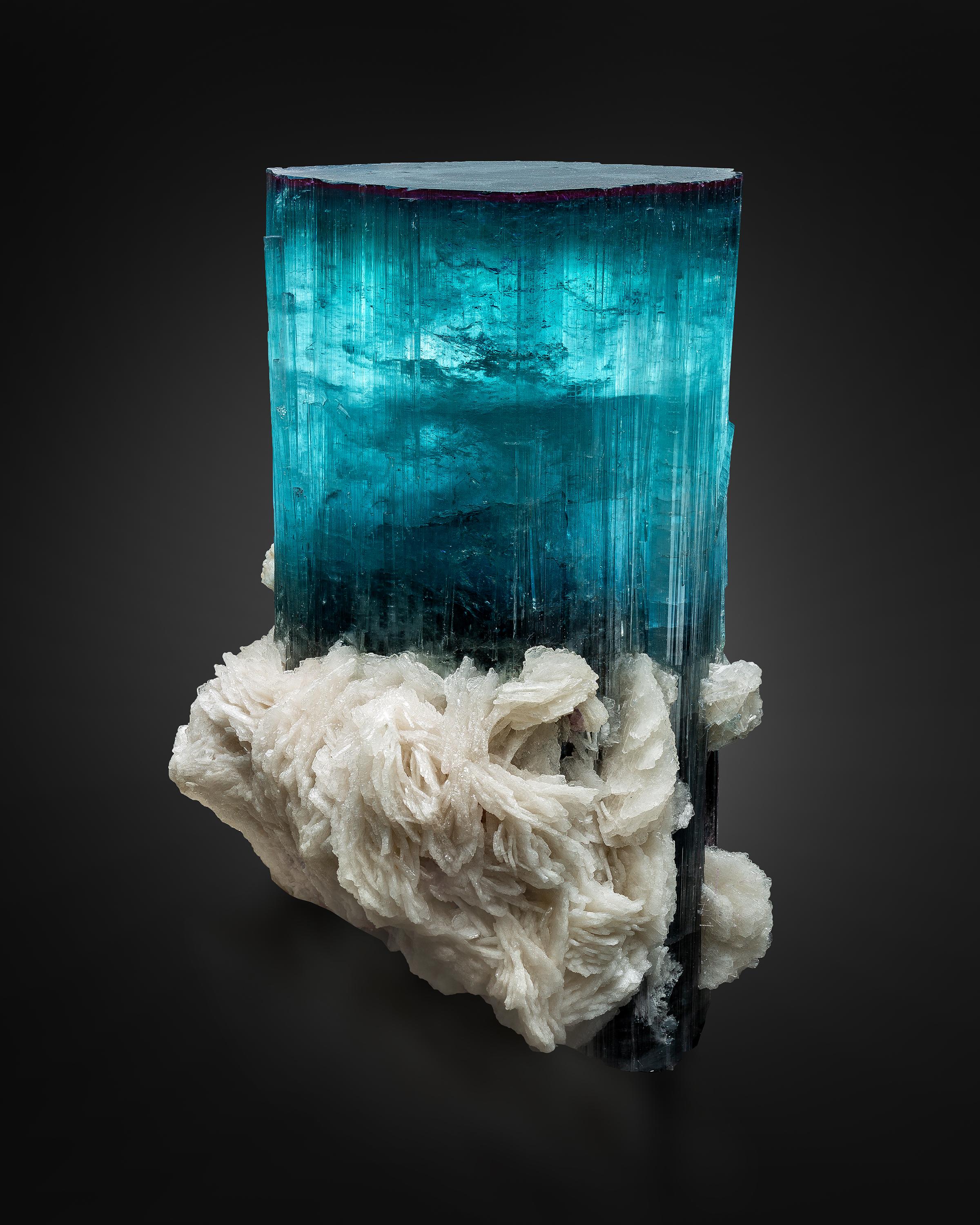 This striking tourmaline crystal has a mesmerizing blue color, a robust size, and sharp form. Upon first glance, the piece appears to have a dark, almost black cap, but when lit, its colors come alive with indigo and violet hues. The crystal’s