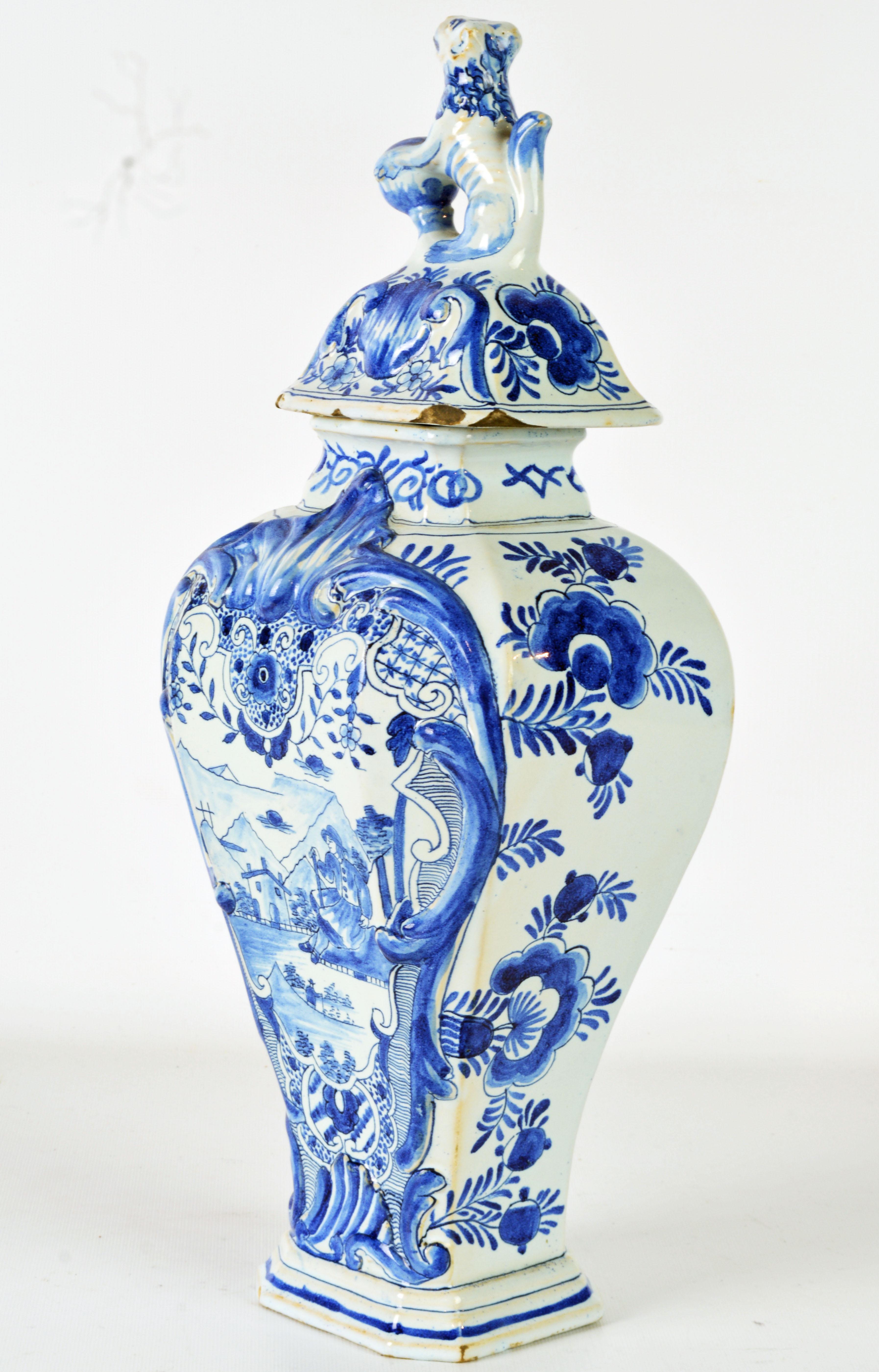 Standing almost 18 inches tall this lovely delft pottery jar features an octagonal cover with a lion clasping a sphere on top above the main baluster shape octagonal body decorated with a mountainous landscape cartouche on the front and stylized