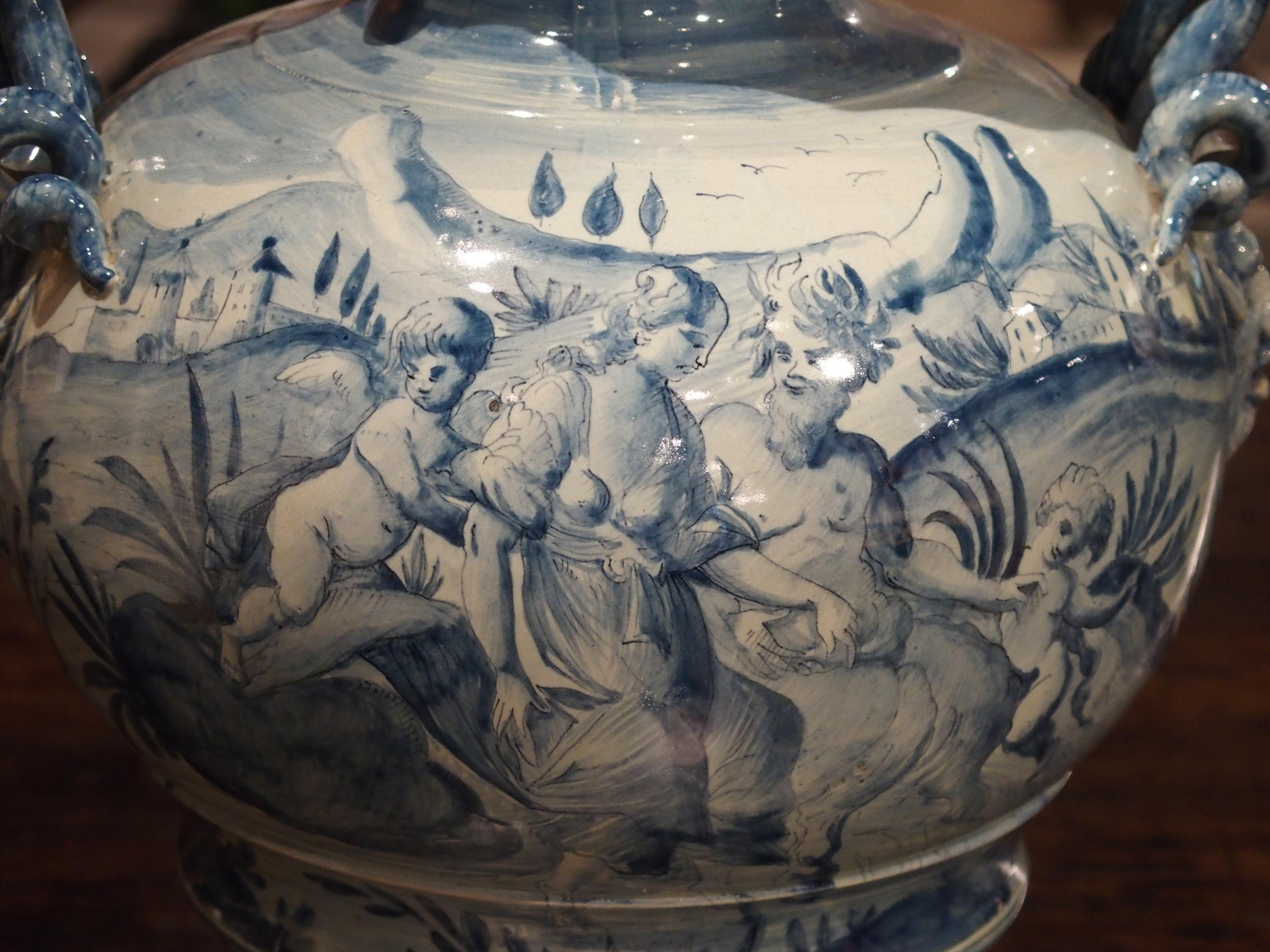 Diese blau-weiße Vase stammt aus der berühmten Majolika-Produktionsstadt Abisola:: Savona:: Italien. Auf der einen Seite ist eine figürliche Szene mit einem Faun:: einer Frau und Putten zu sehen. Im Hintergrund sind Schlösser und Berge zu sehen. Die