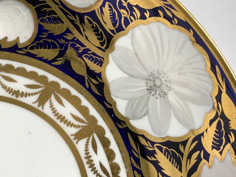 This exquisite Regency period dish is painted in underglaze deep blue cobalt. Because the porcelain is translucent the intensity of the blue varies in the light. The blue ground is decorated with golden leaves and white peonies and daisies. The