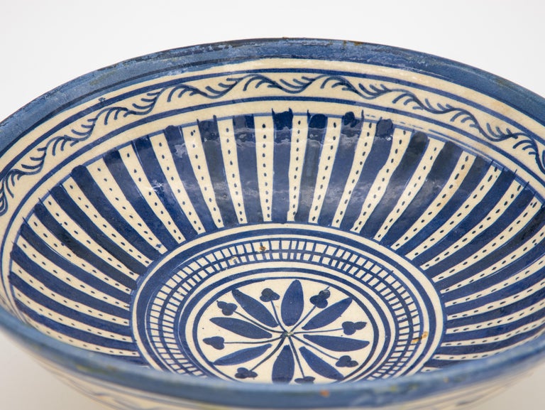 A beautiful handpainted Fes ceramic platter or bowl brightly colored in blue and white. Featuring stripes, dots, a central flower, and a branch border. This Moroccan bowl made in Fes is called a Gothar and was made at the end of 19th century. Wear