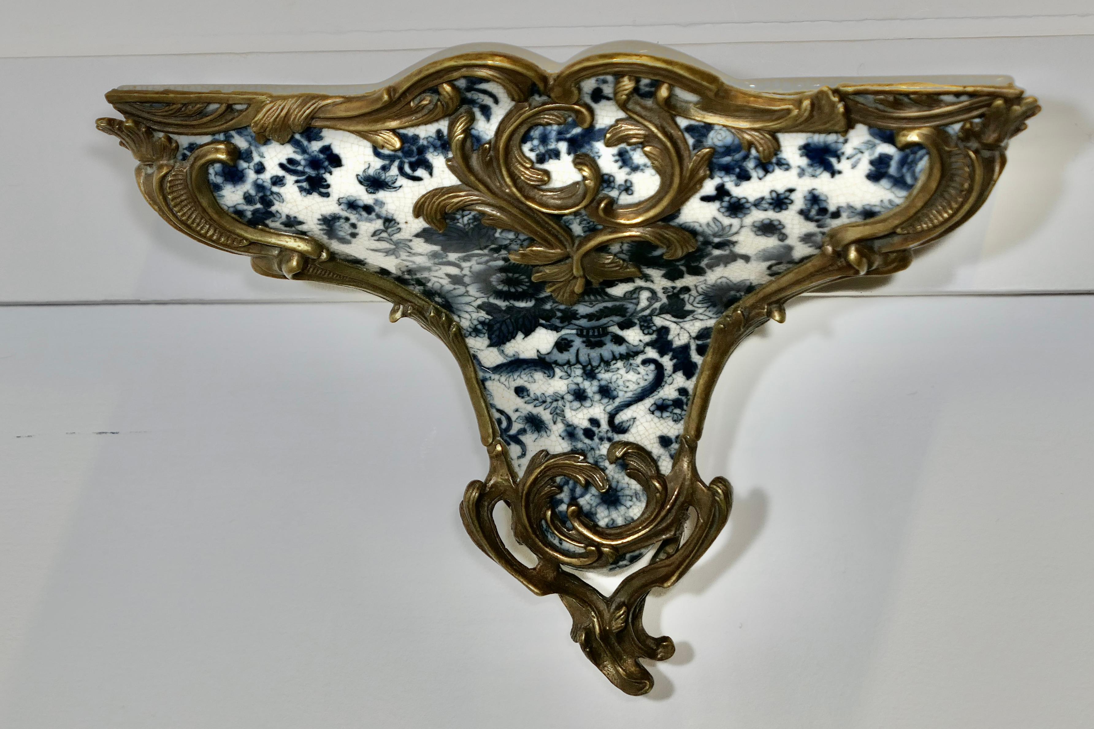 Support mural bleu et blanc en céramique et bronze doré 

Il s'agit d'une pièce magnifique qui présente un décor floral en céramique Delft souligné d'une bordure en bronze doré, qui sert manifestement de support au support tout en le décorant.  

Le