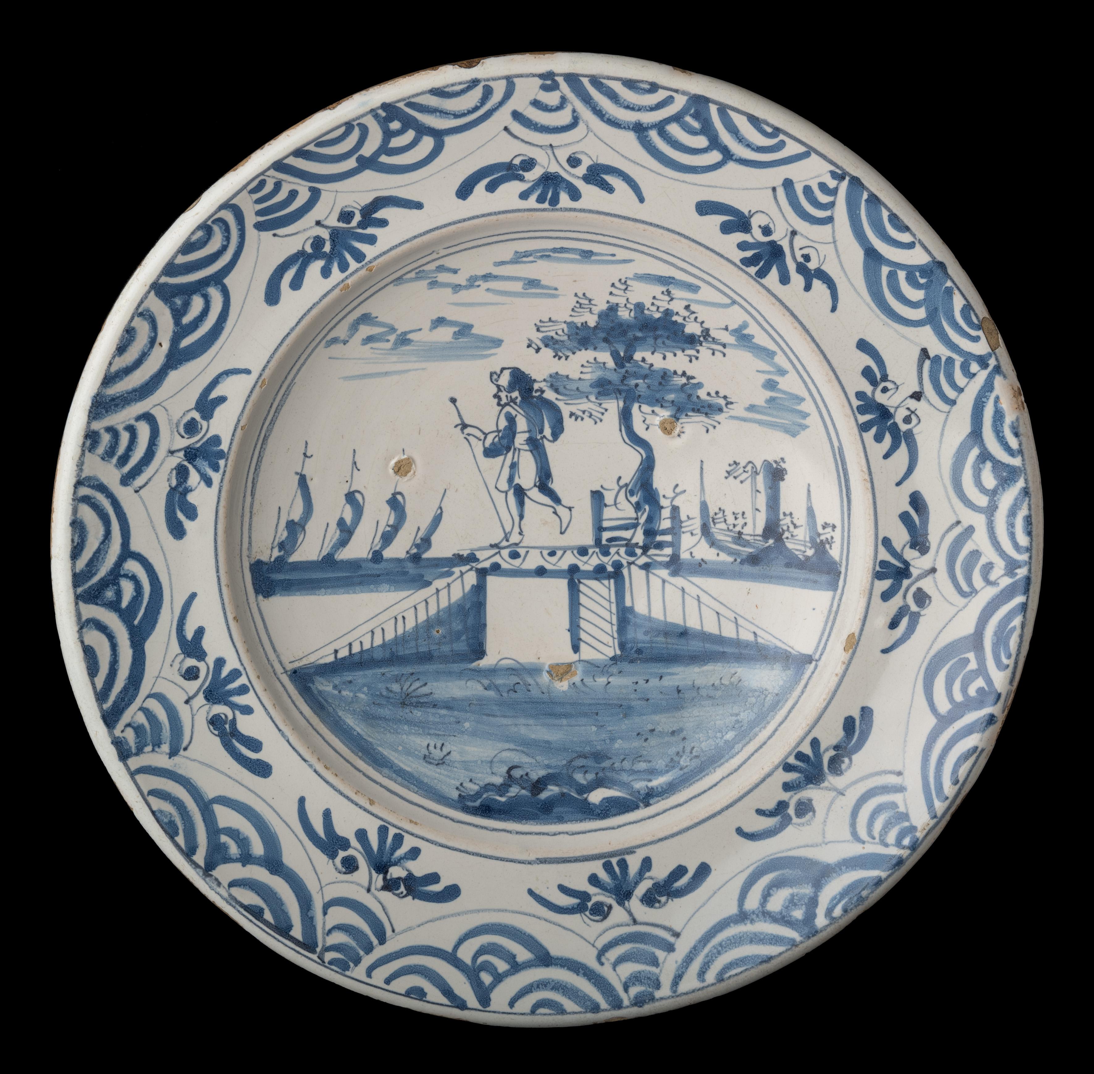 Blue and white charger with a shepherd in a landscape Delft, 1670-1700

The charger has a wide-spreading flange and is painted in blue with a shepherd in a water landscape. 
He wears a hat and carries a knapsack, and holds a long staff in his