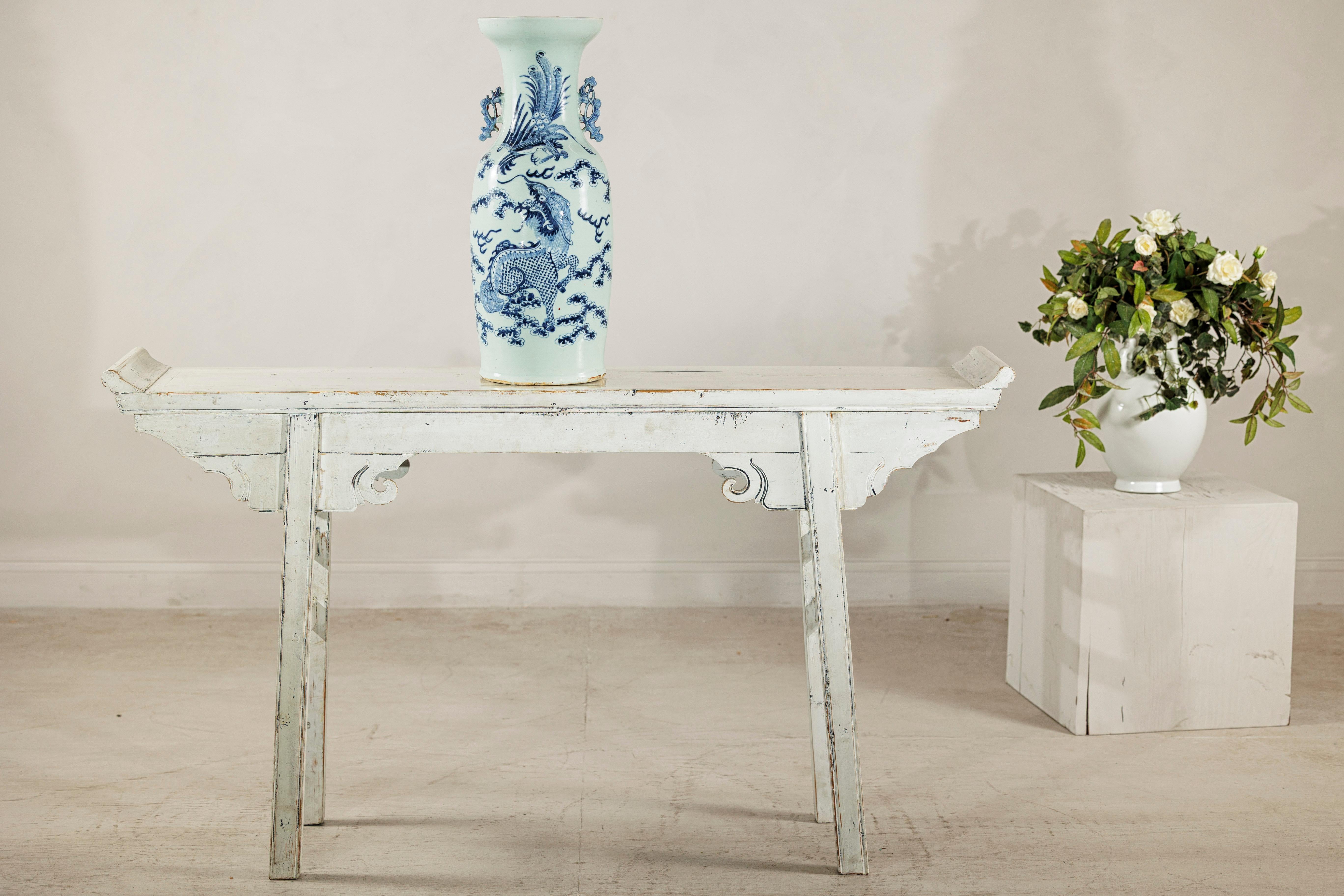 Ce grand vase d'autel en porcelaine chinoise est décoré en bleu et blanc classique avec une subtile teinte céladon, et présente un élégant bord évasé mesurant environ 8 pouces de diamètre. La surface du vase représente une scène dynamique d'un