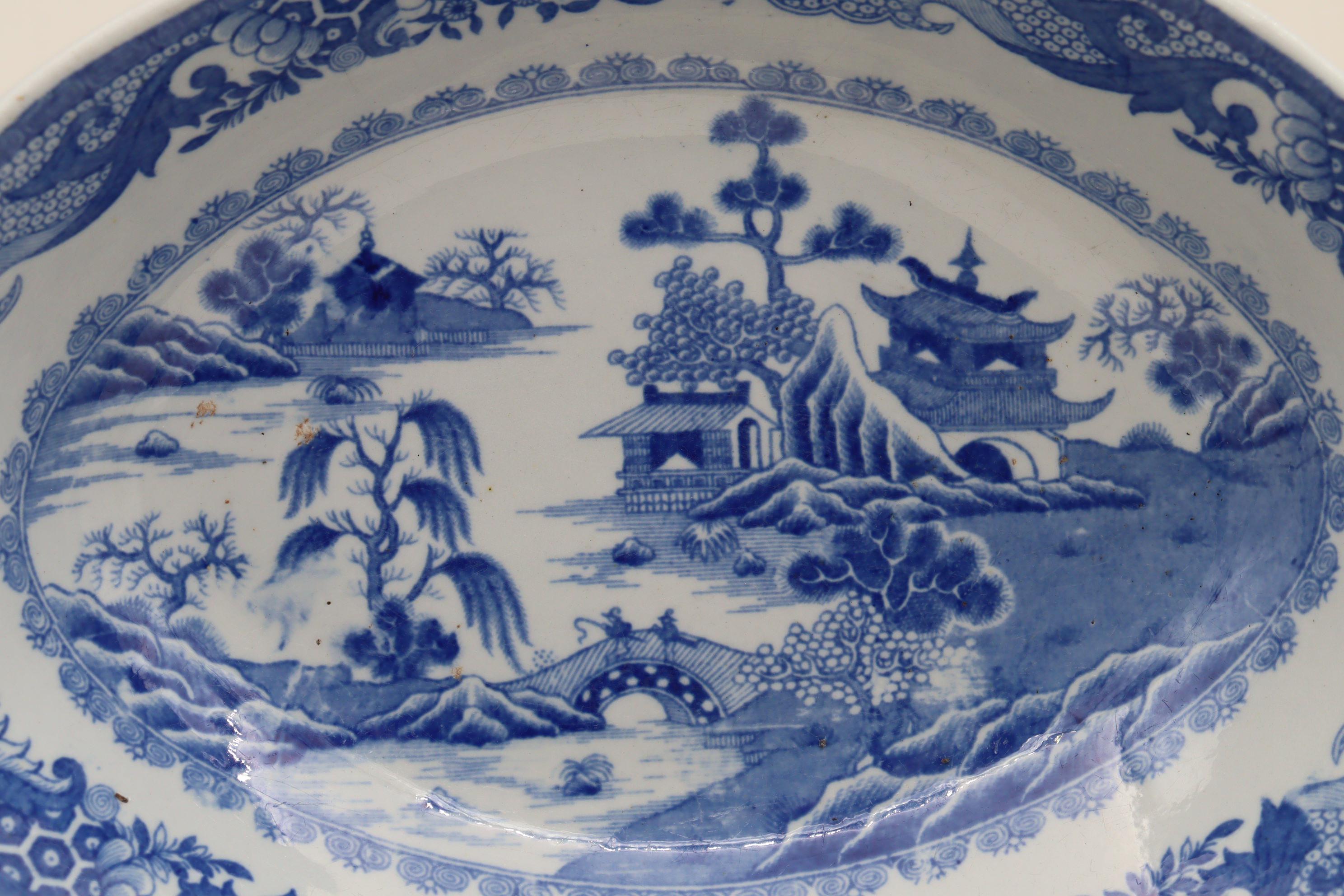 This low oval, almost canoe shaped blue and white bowl is decorated with a chinese style transfer print under a pearlware glaze and measures 277 mm (10.75 inches) in length, 207 mm (8.25 inches) in width and stands 68 mm (2.75 inches) high. It is