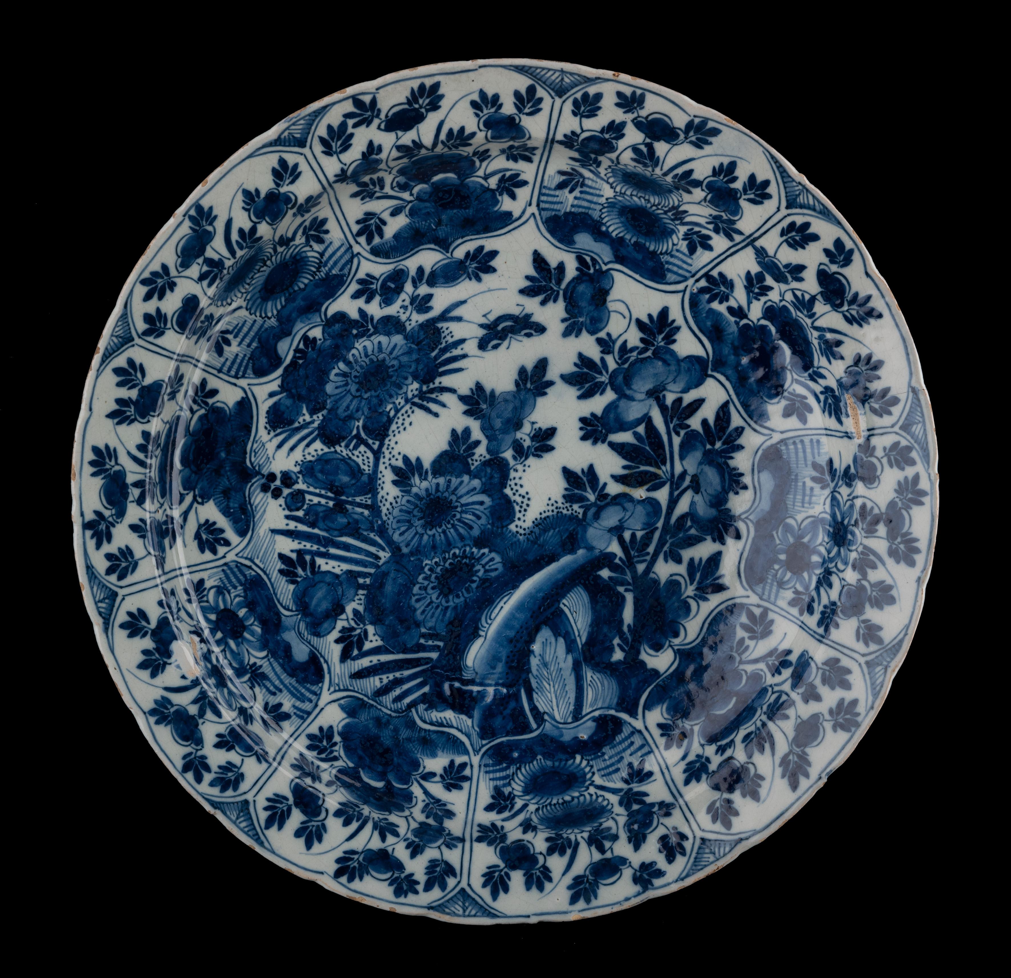 Blue and white chinoiserie dish Delft, 1691-1724
The Metal Pot pottery
Mark: LVE, period of Lambertus van Eenhoorn (1691-1724) 

The dish has a narrow, flat flange and is painted in blue with a floral chinoiserie decor of plants and flowers issuing