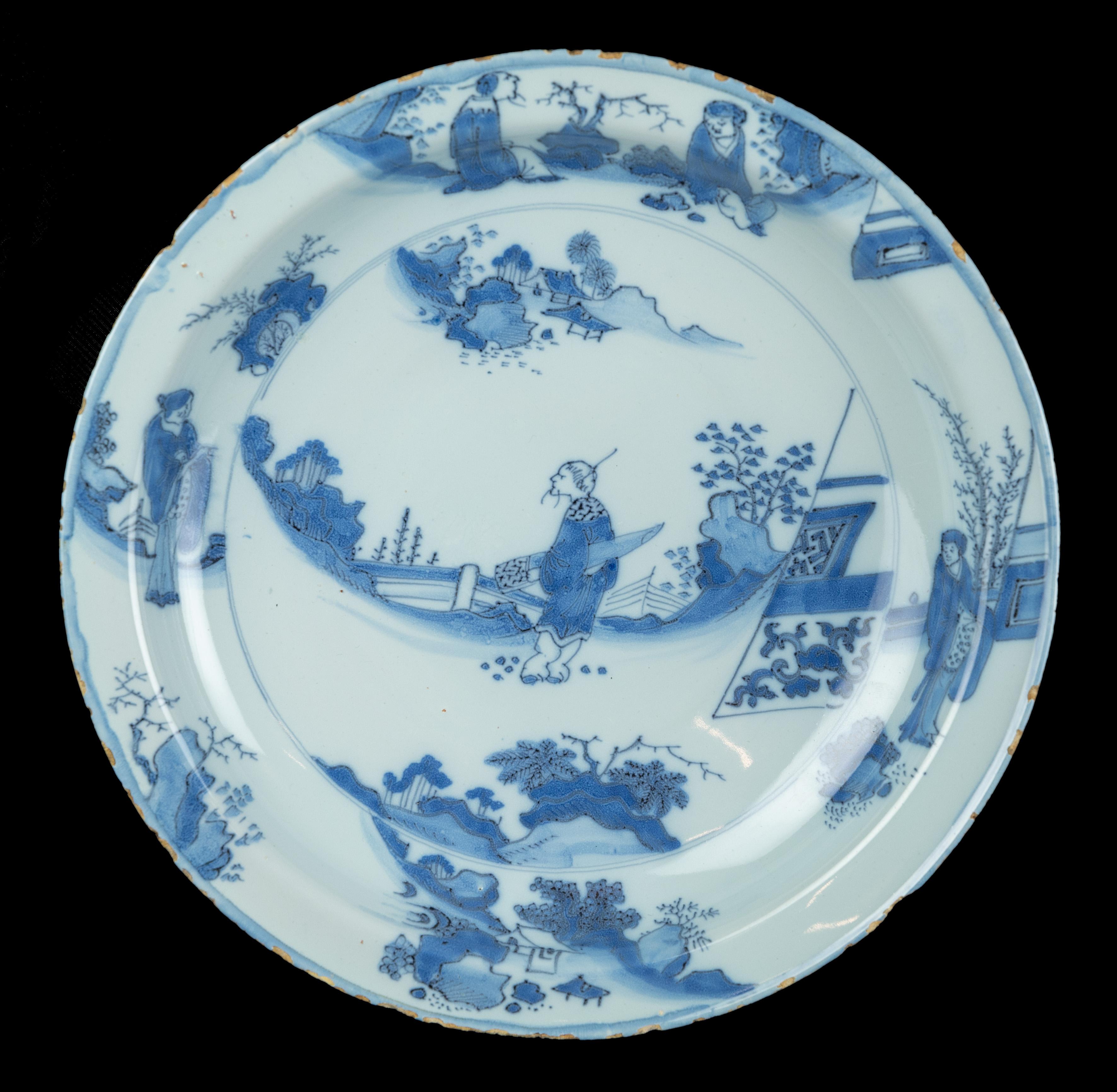 The blue and white dish has a narrow, flat flange and is painted in the centre with a Chinese figure in an oriental garden landscape in a double circle. The brushwork is executed in blue within purple outlining on a light blue-coloured tin-glaze.