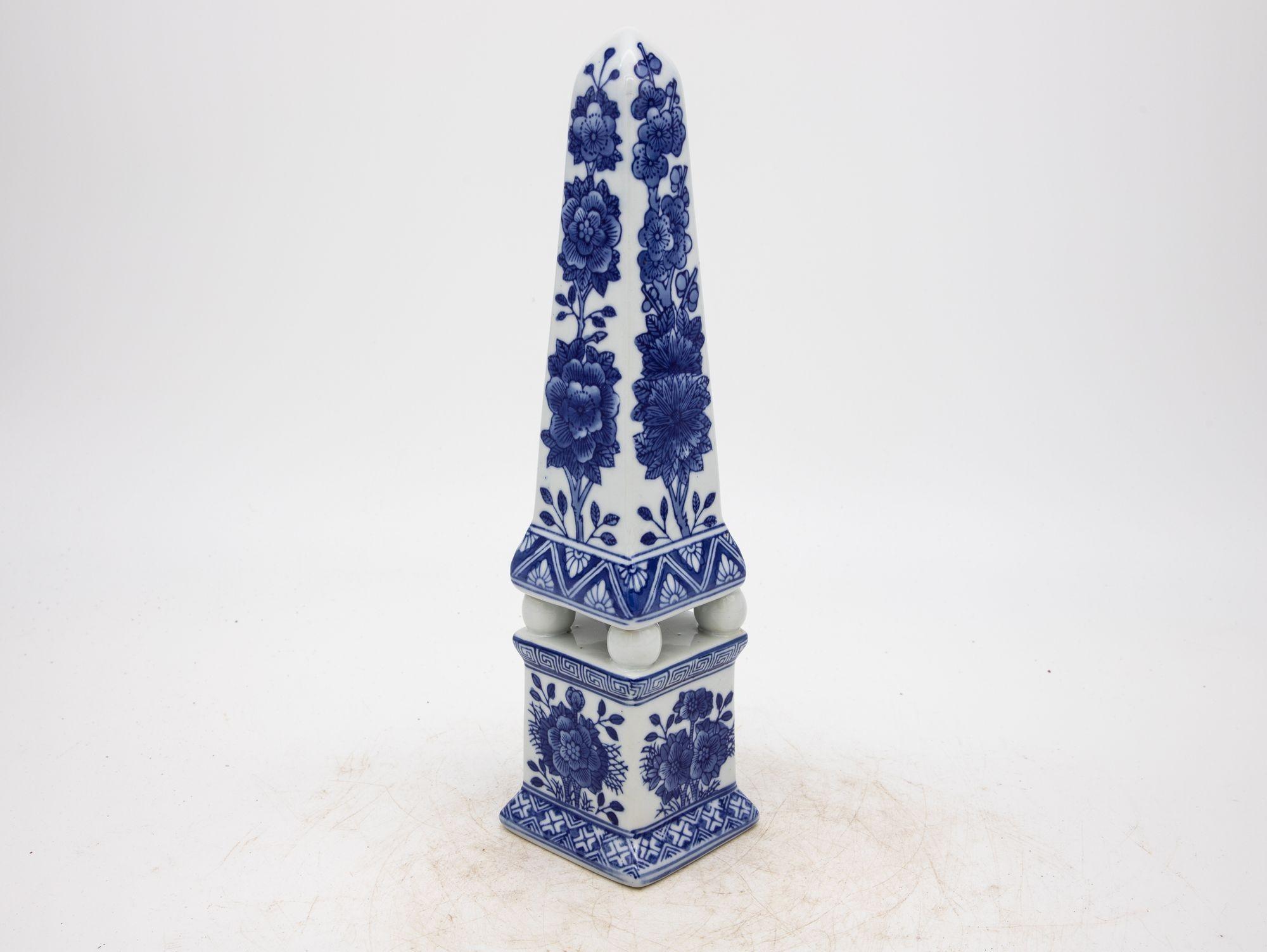 Elegance takes a distinctive form in this blue and white chinoiserie ceramic obelisk. The intricate detailing captures the essence of traditional East Asian artistry. Delicate strokes of cobalt blue dance upon a pristine white background, portraying