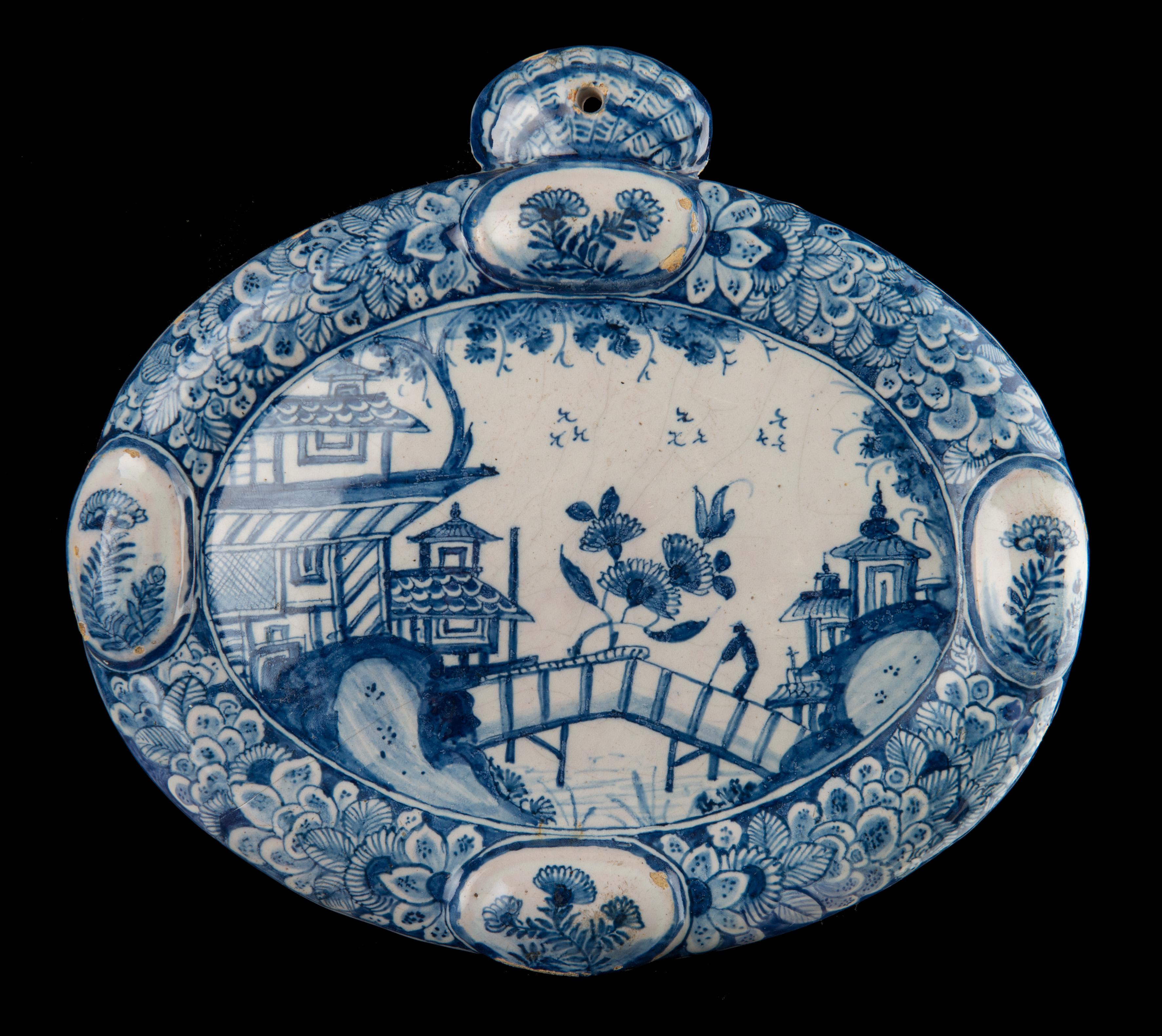 Blue and white chinoiserie plaque. Delft, 1740-1760.

The oval blue and white plaque has a molded rim with four raised, oval cartouches. At the top a shell-shaped suspension loophole is molded. The plaque is painted with a chinoiserie water