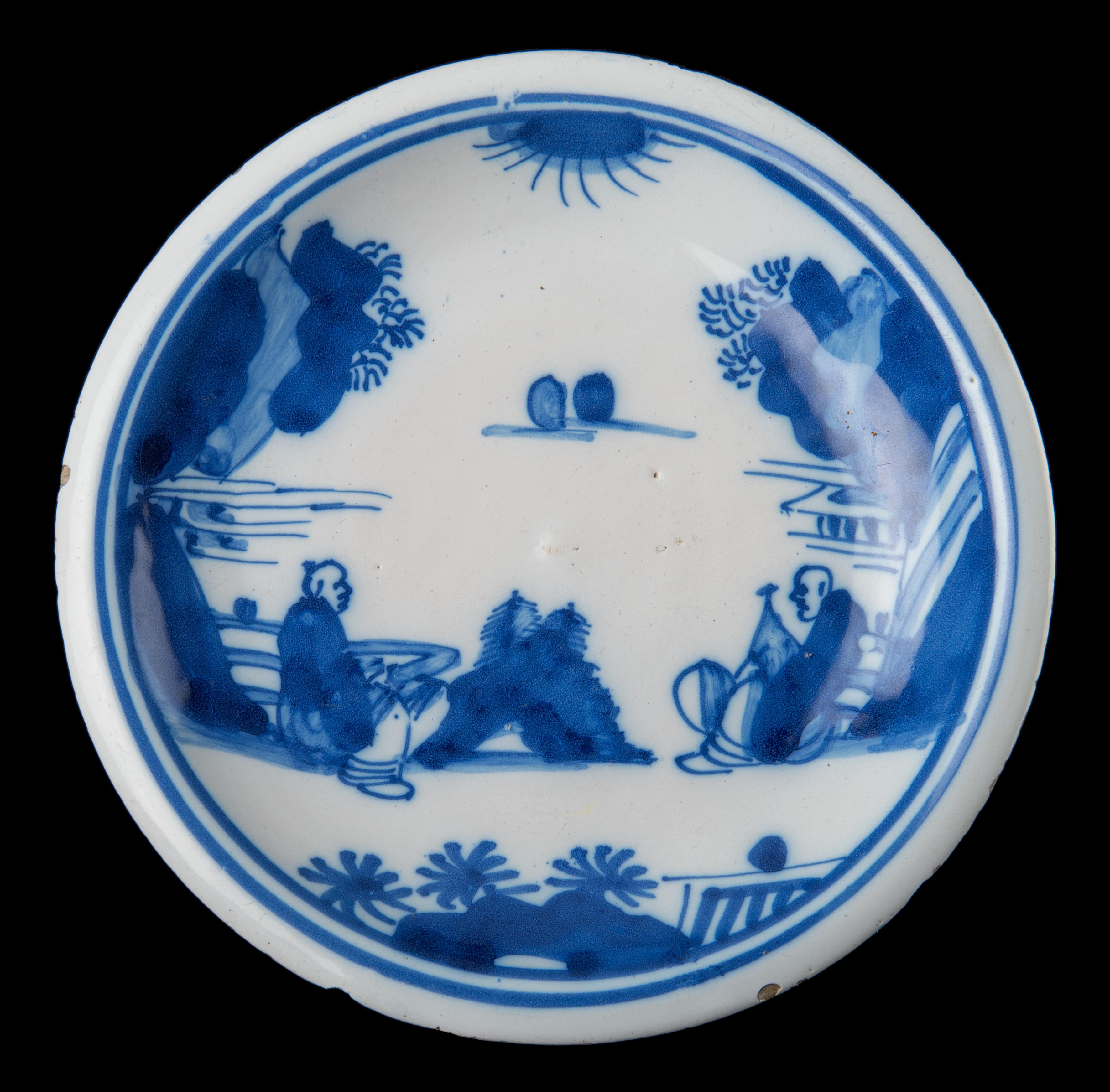 Blue and white plate with a chinoiserie landscape with two sitting Chinese figures, within a double circle. The back of the plate is painted with the number 5, and the foot rim is pierced. The decoration is inspired by Chinese porcelain from the