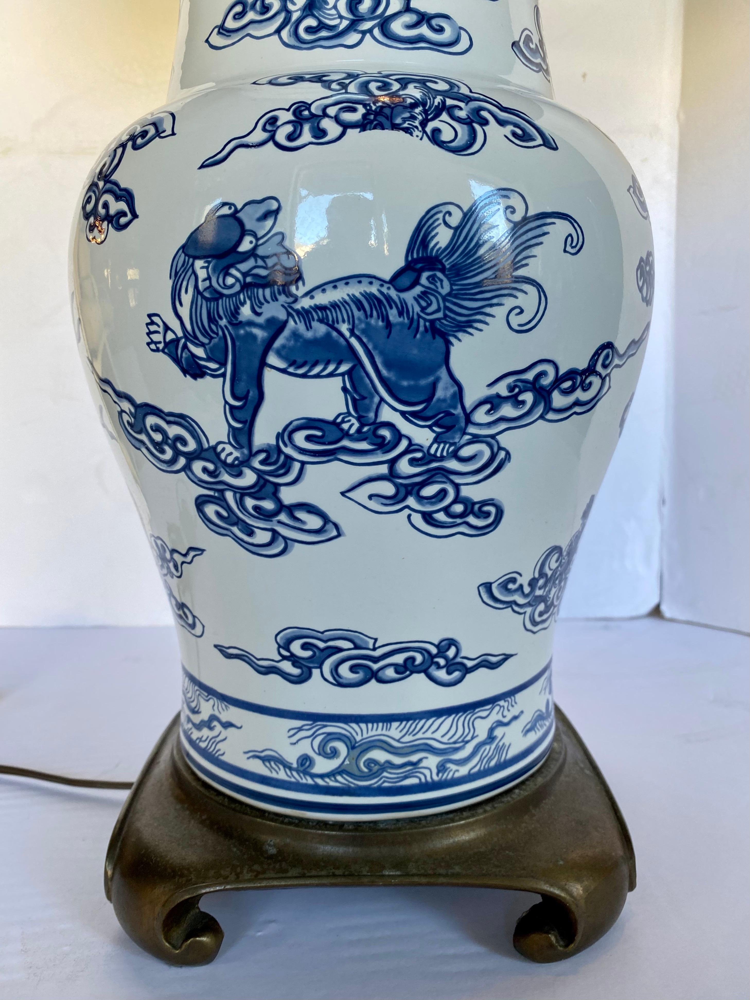 Large chinoiserie style blue and white porcelain ginger jar table lamp mounted on Ming style brass base. Classic urn vase shaped body is decorated with Chinese motifs, foo dogs and blue coral. Lamp shade not included.