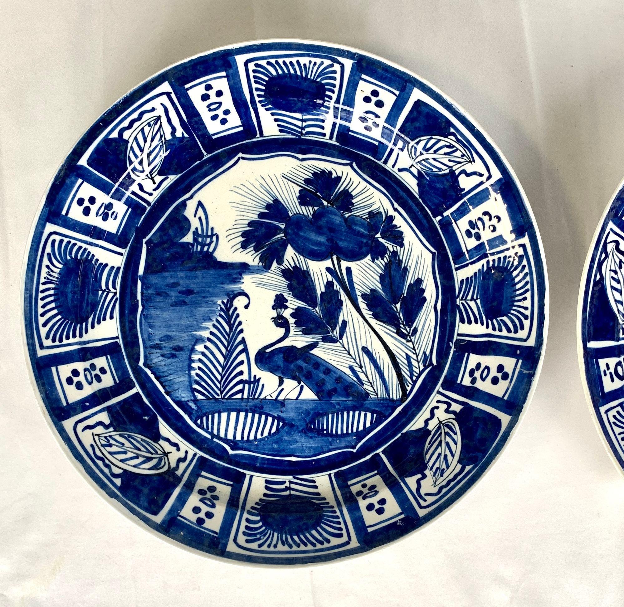 This pair of mid-18th-century Dutch Delft chargers is handpainted in several shades of cobalt blue.
The viewer is drawn to the lovely scene in the center of each charger, which shows an elegant peacock in a flowery garden near water.
The wide rim
