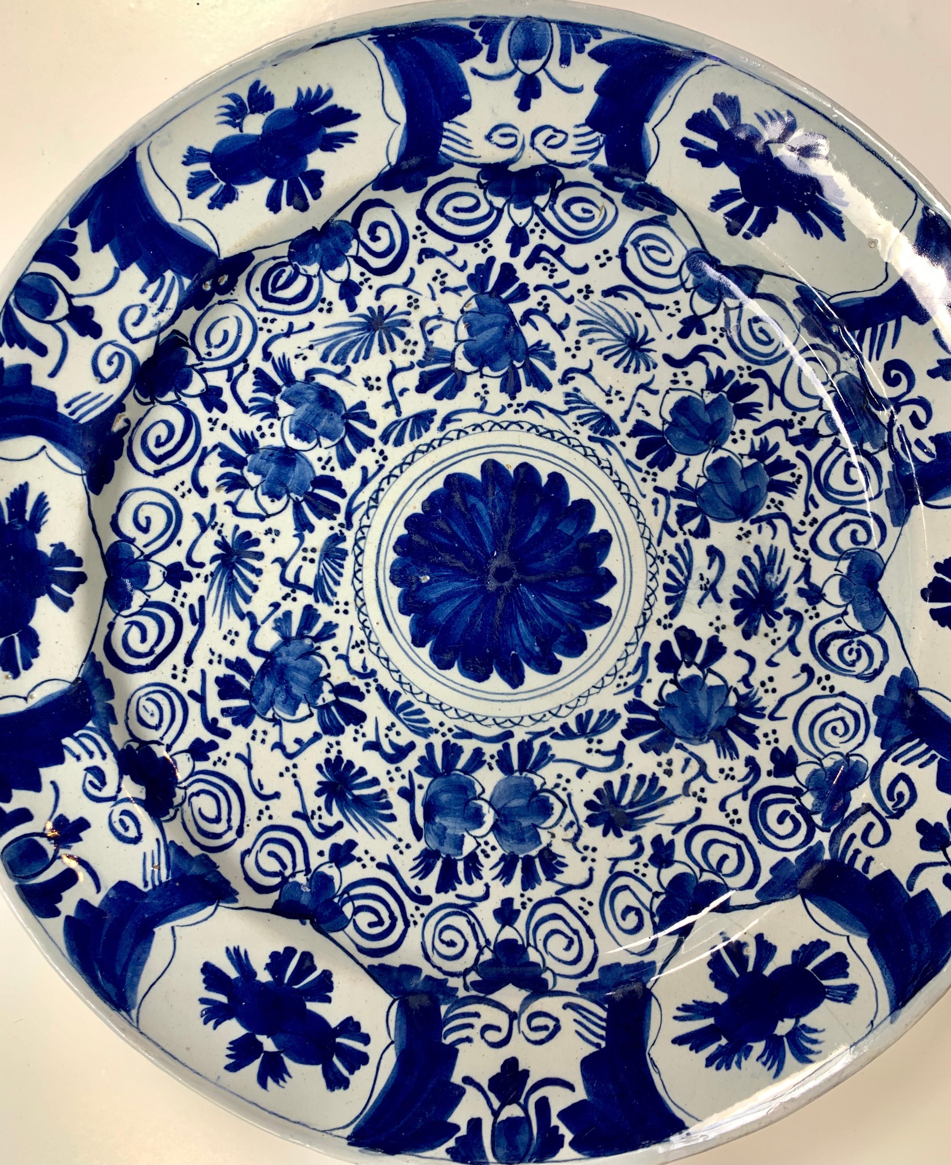 This blue and white Dutch Delft charger was hand-painted circa 1780.
 The center of the charger is decorated with a large flower. Beyond the center, we see flowers that seem to follow one another around in a circle actively. The vibrant decoration