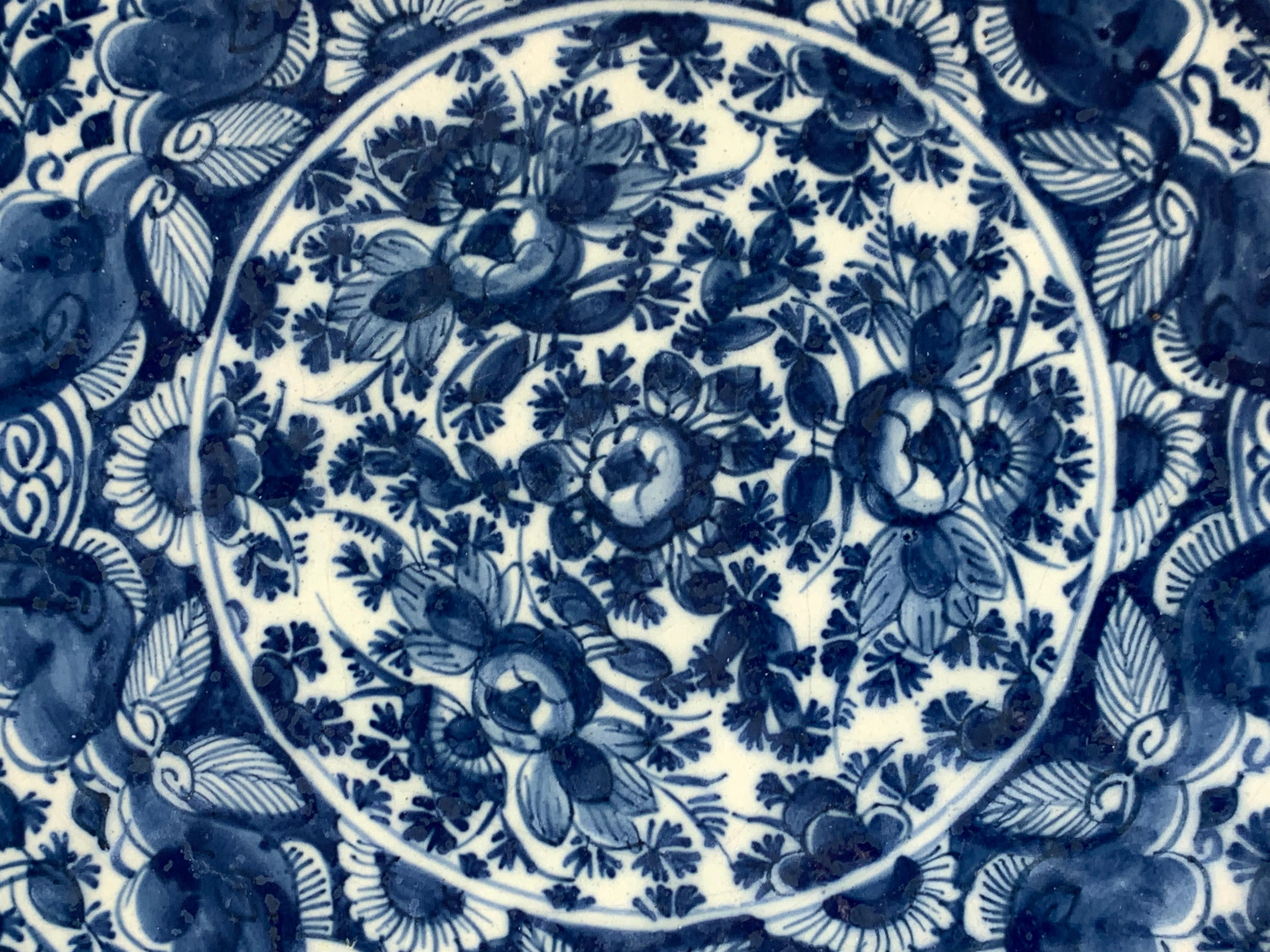 The entire surface of this blue and white Dutch Delft charger is covered in deep beautiful cobalt blue coloring. 
The center of the charger is filled with lovely hand-painted peonies, while the wide border is painted with a net-like pattern of