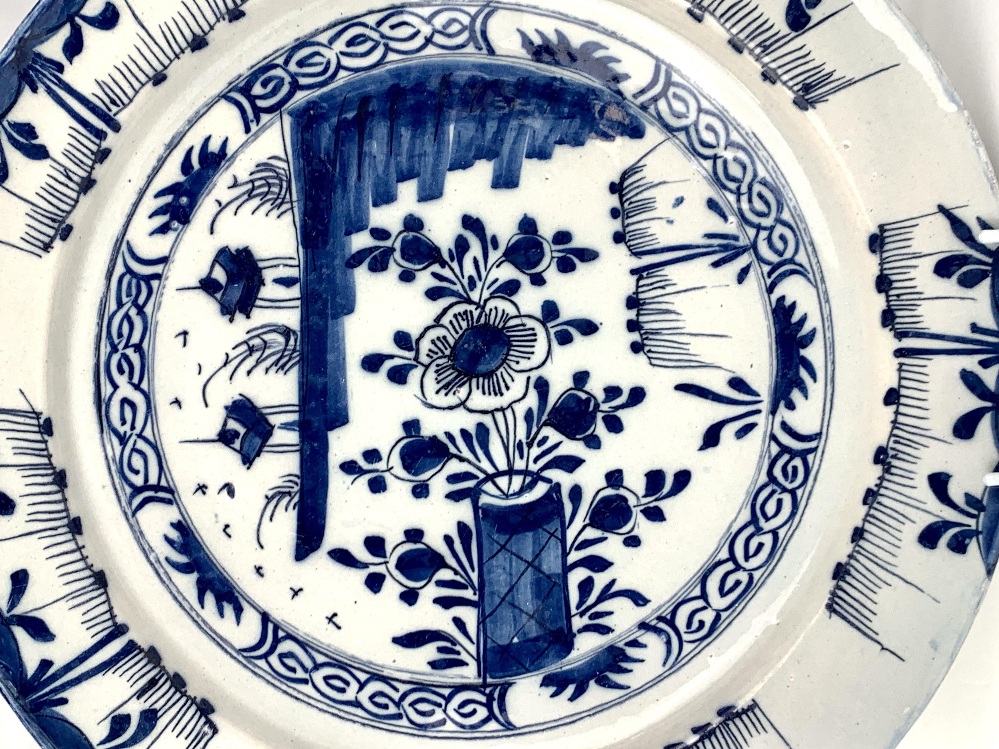 This blue and white Dutch Delft charger shows a chinoiserie scene in a lovely naive style.
The chinoiserie scene in the center of the charger includes three unique viewpoints.
On one side, we see a flower and buds in a vase.
On the other side, we