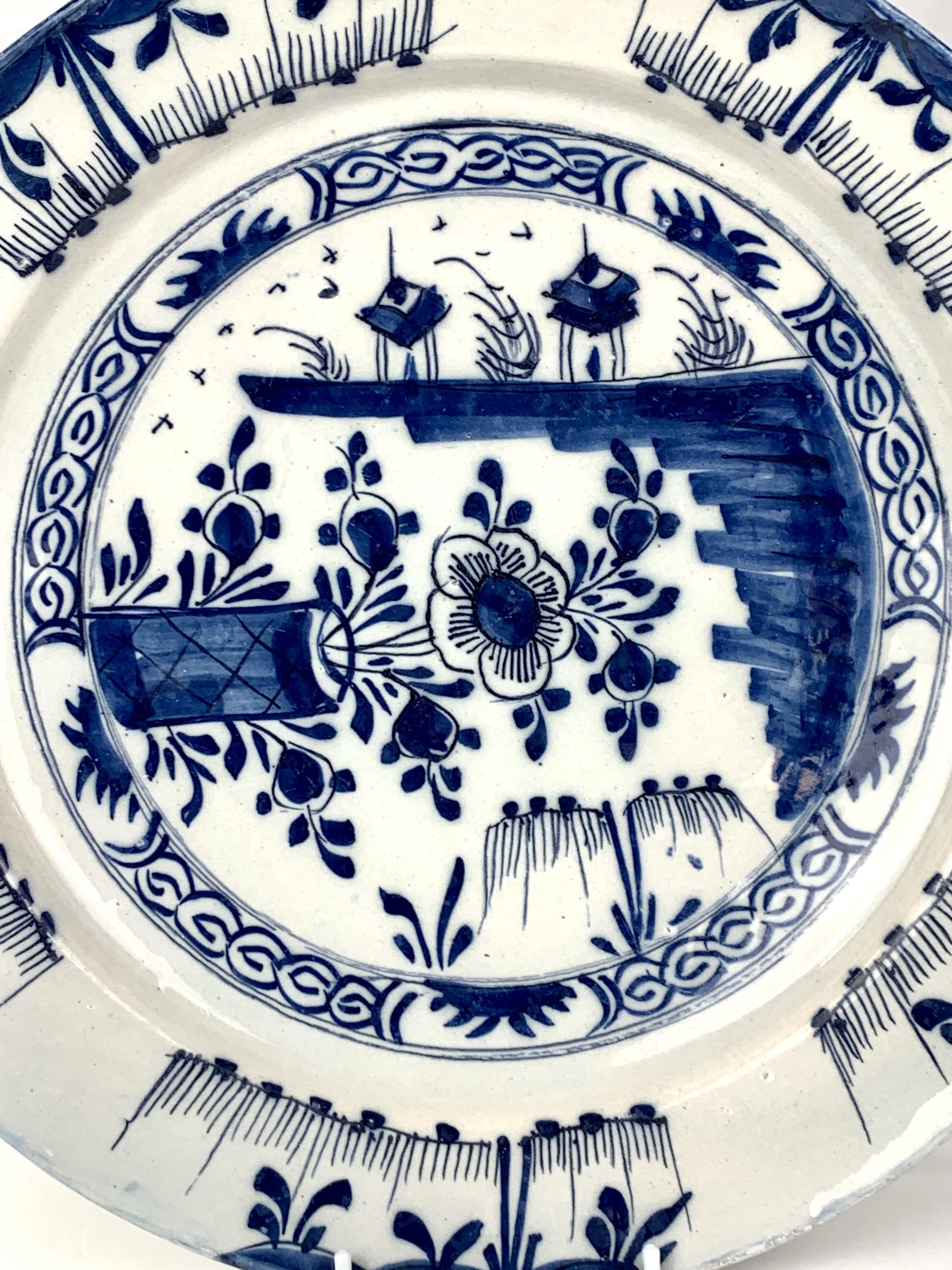 This blue and white Dutch Delft charger shows a chinoiserie scene in a lovely naive style.
The chinoiserie scene in the center of the charger includes three unique viewpoints.
On one side, we see a flower and buds in a vase.
On the other side, we