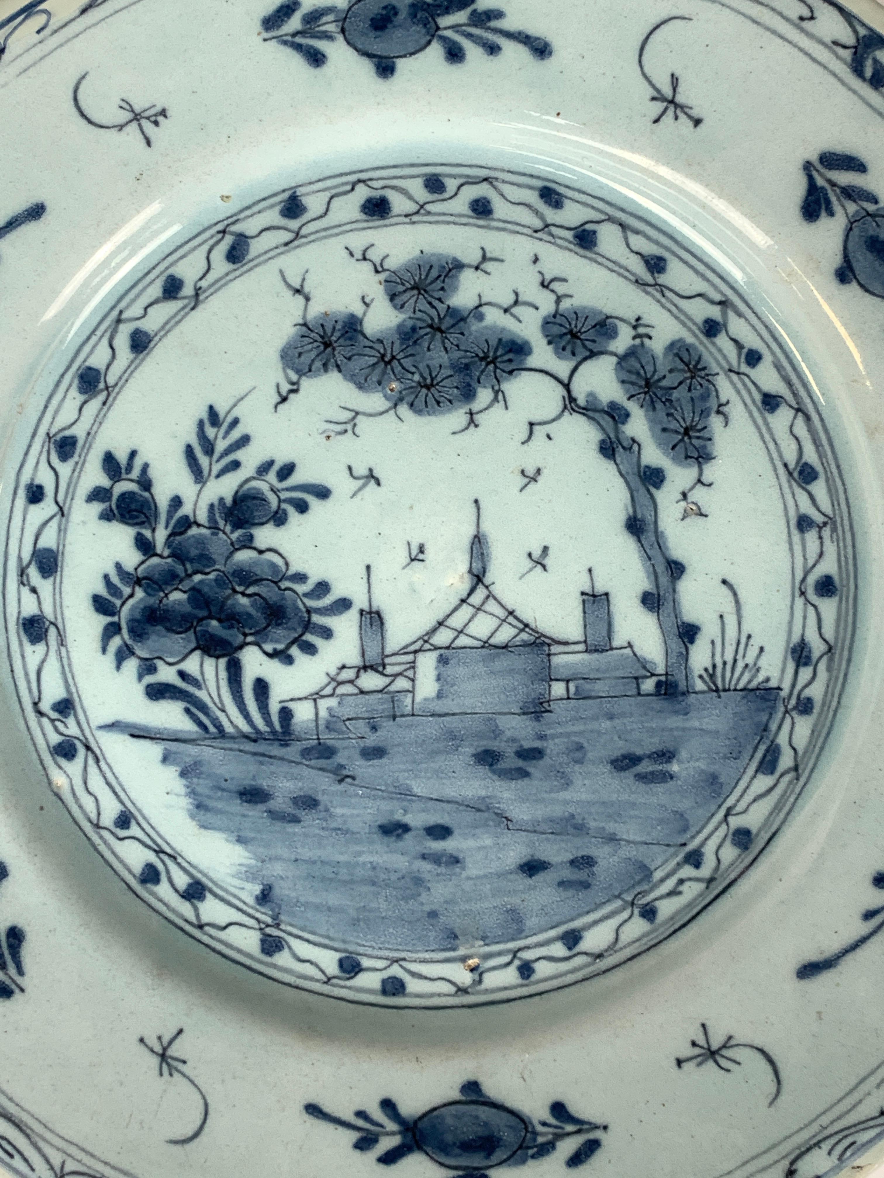 This Delft blue and white dish was hand-painted in England in the 18th century circa 1760. 
The painting is quite naive but eye-catching. 
In the center, we see a large blue ground before three homes, each with a chimney. 
To the left, we see a