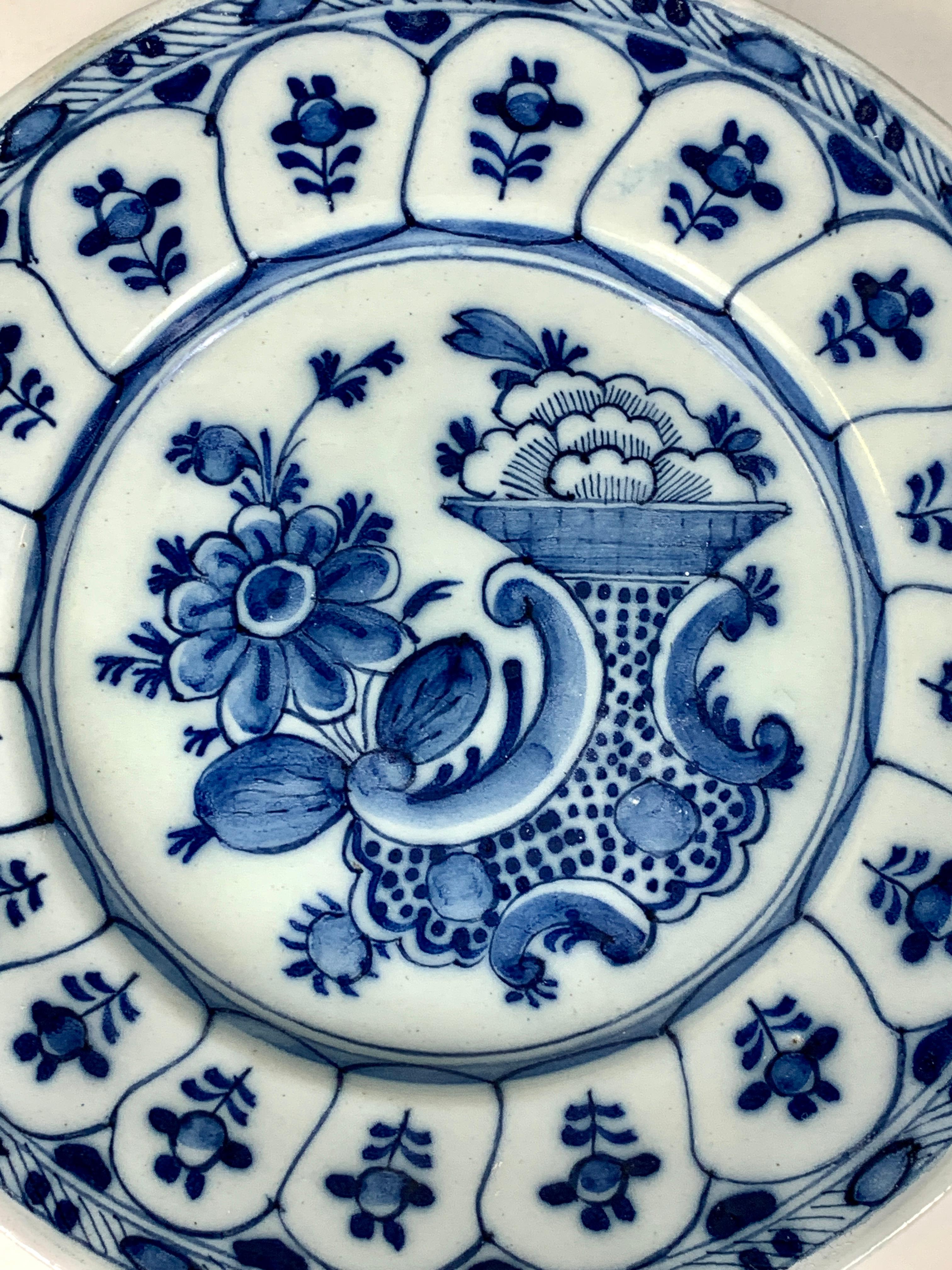 This blue and white hand-painted Dutch Delft dish was made in the Netherlands in the 18th century, circa 1780. 
The composition has excellent movement. The center shows flowers and a Rococo vase with curving outlines. 
Seventeen panels encircle the