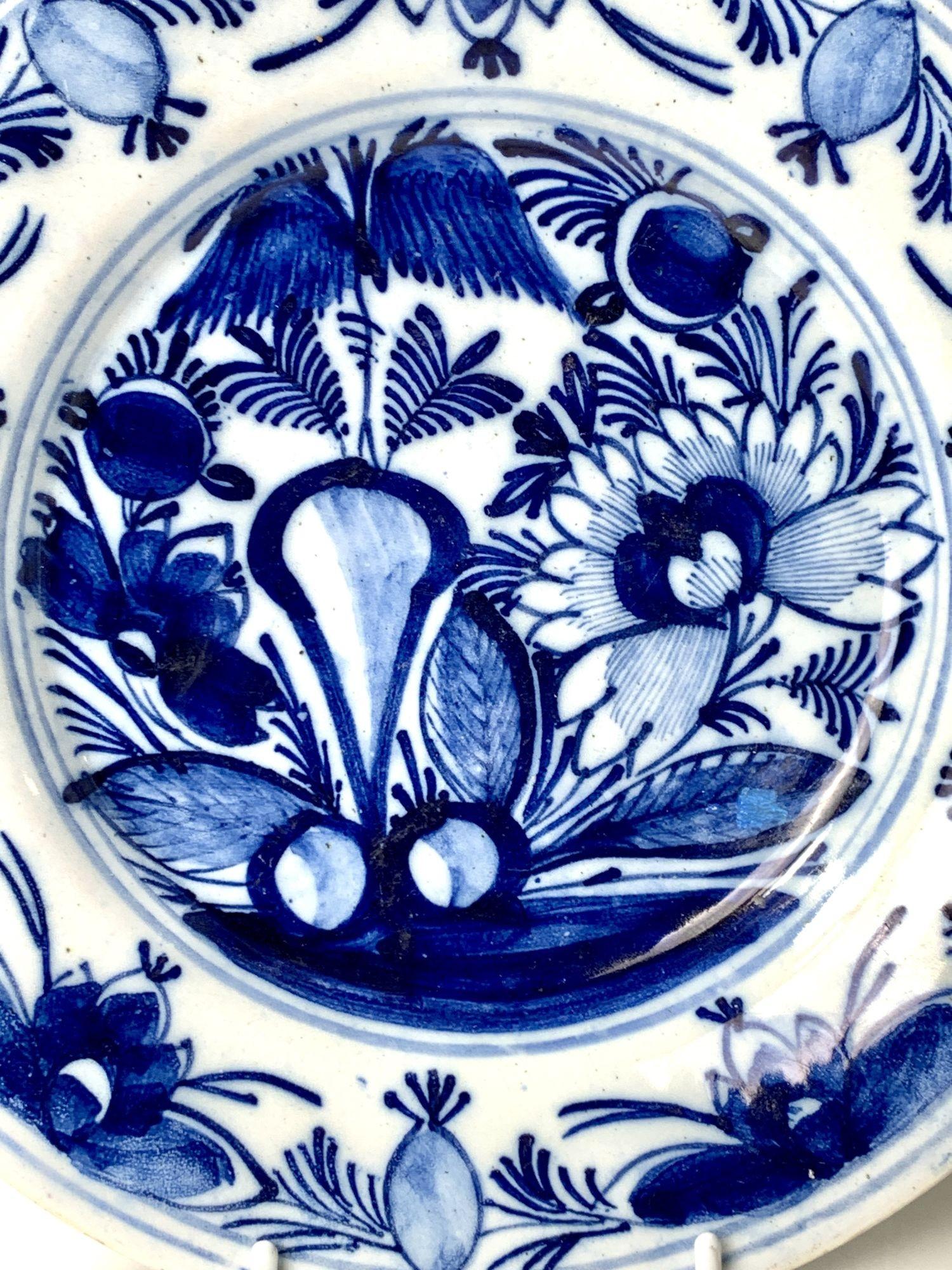 At the center of this lovely hand-painted blue and white Delft dish is a traditional chinoiserie view of a garden. 
We see an oversized peony, a willow tree, and rockwork. The wide border shows water lilies and flower buds. 
The artist used cobalt
