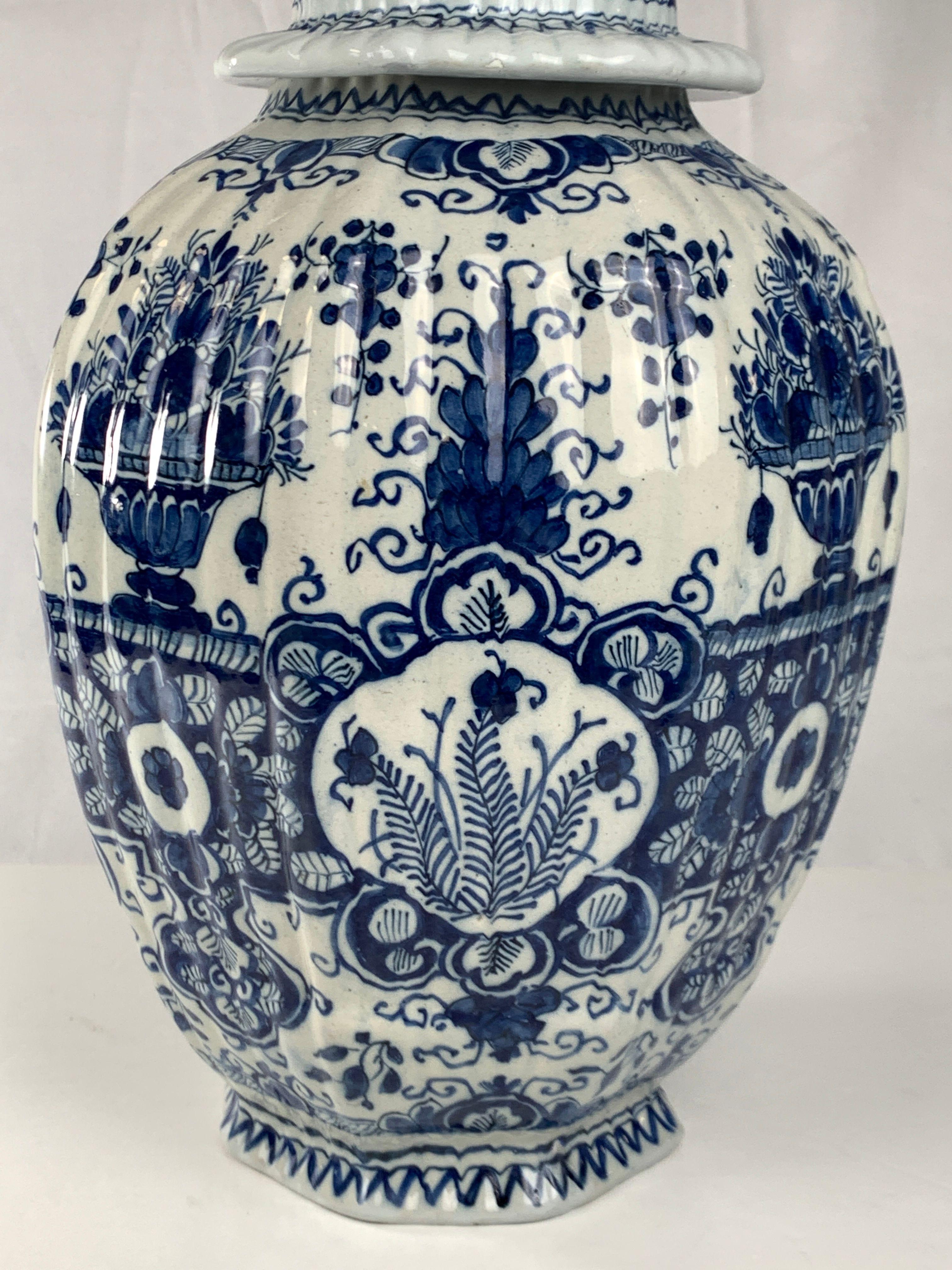 This large blue and white Delft jar is hand-painted, showing exquisite flower-filled baskets on a white tin-glazed ground.
We see sunflowers and tulips overflowing baskets alongside floral decoration with scrolling vines.
The ribbed body sits on a