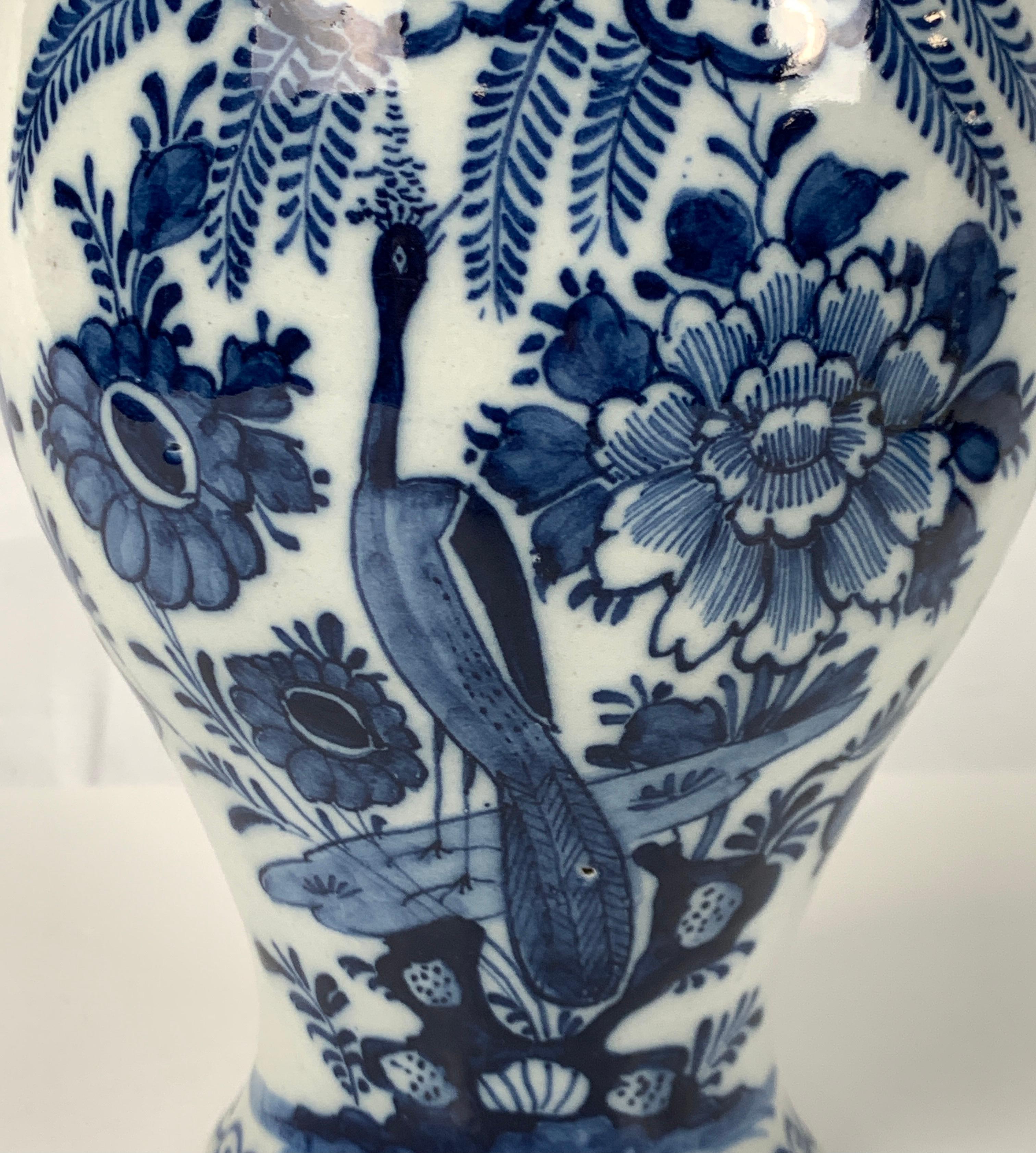 A blue and white Dutch Delft mantle jar hand-painted in exquisite deep cobalt blue. 
We see a peacock in a garden filled with flowers and ferns. 
The cover is similarly decorated and topped with a traditional round knop covered in blue.
Made in