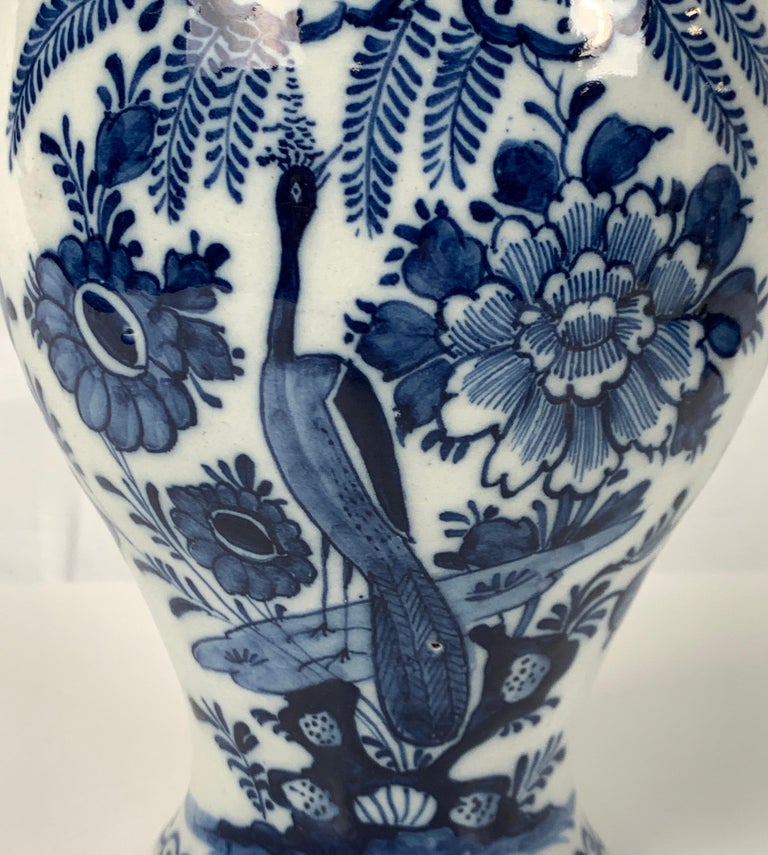 A blue and white Dutch Delft mantle jar hand-painted in exquisite deep cobalt blue. 
We see a peacock in a garden filled with flowers and ferns. 
The cover is similarly decorated and topped with a traditional round knop covered in blue.
Made in
