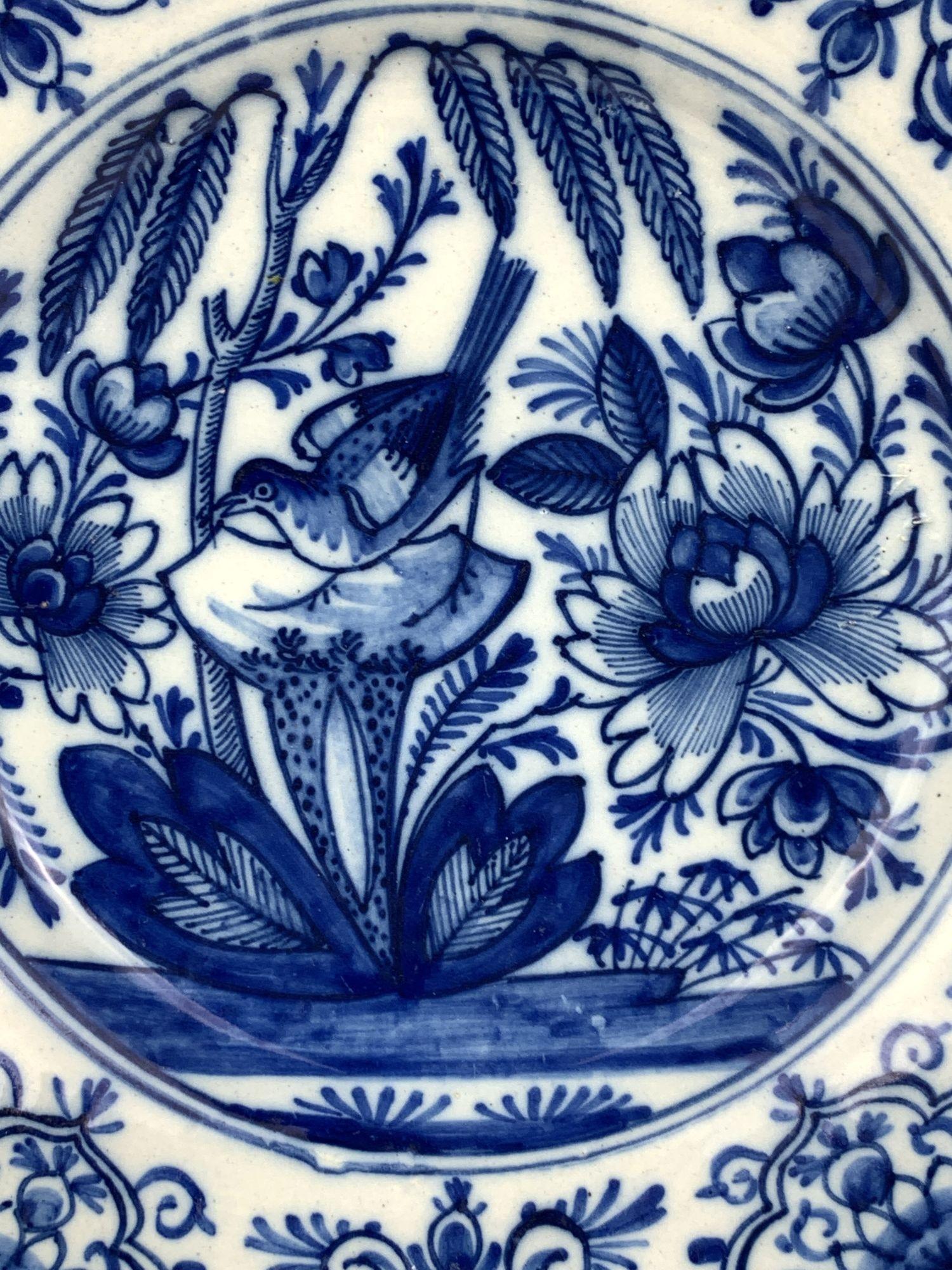 This Delft dish is hand-painted in fabulous, intense cobalt blue. 
The center shows a lovely garden with a songbird among blooming flowers and a willow tree with its branches draped over the garden.
The border of the dish is filled with floral