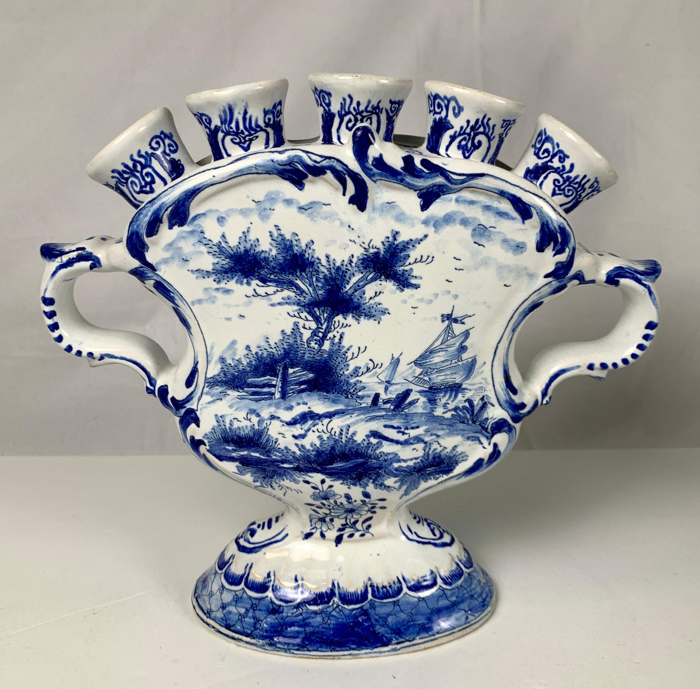 This blue and white Dutch Delft tulipiere or tulip holder shows a lovely romantic scene. 
We see a shepherdess delicately walking onto a stepping stone at the stream's edge.
The reverse shows sandy dunes and sailing ships gliding by in the water