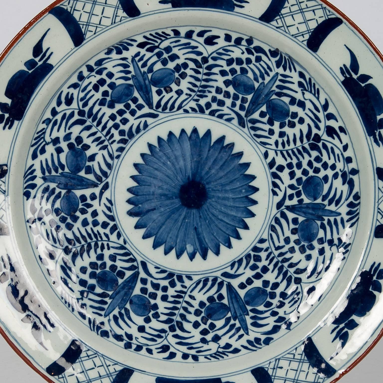 A large Dutch delft blue and white charger with deep cobalt blue decoration. The charger features a large chrysanthemum in the center around which are scrolling vines and tulip buds. Along the border are naive floral designs painted in the flat leaf