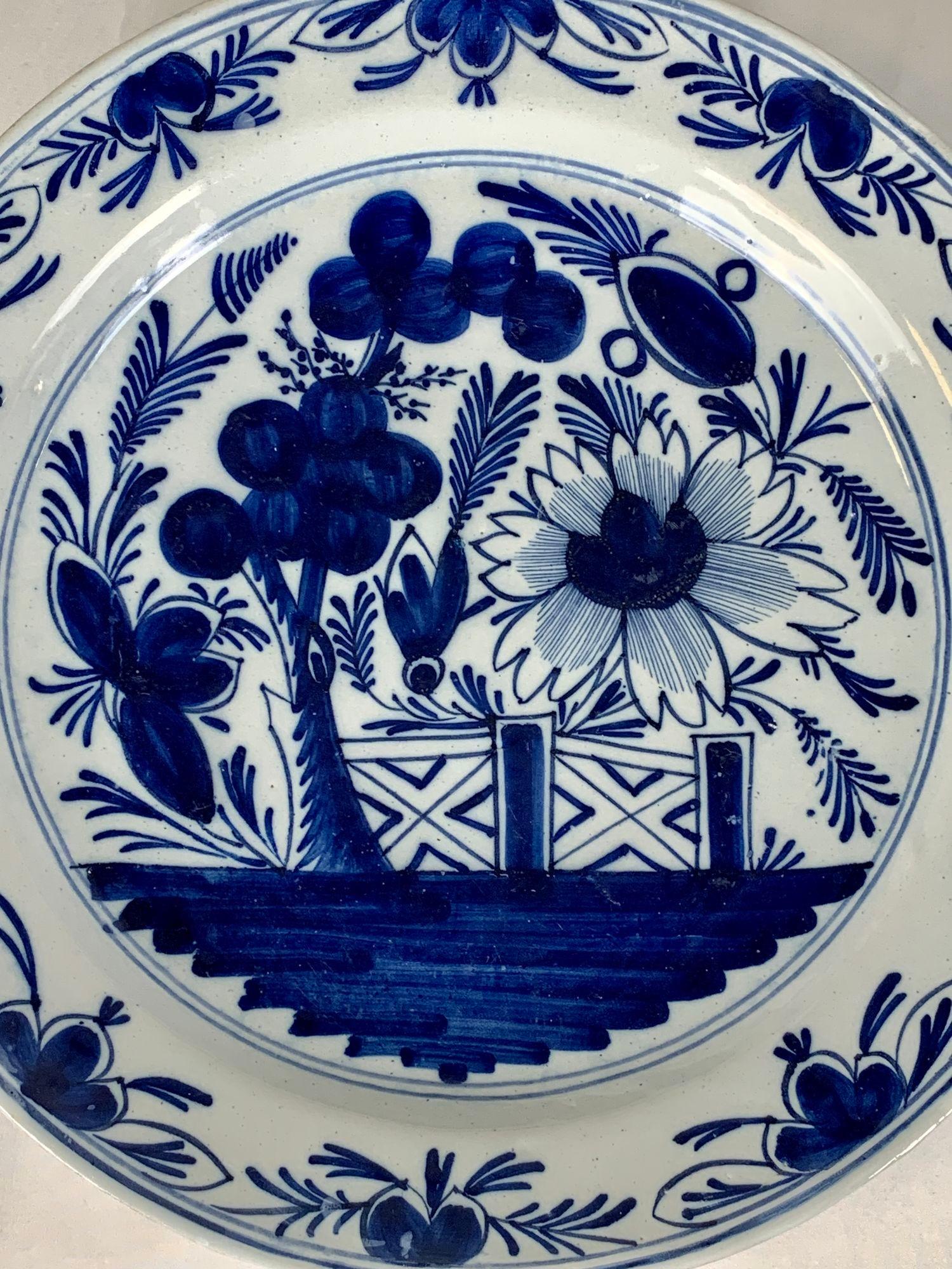 Made in the Netherlands circa 1800, this antique blue and white Dutch Delft charger has beautiful cobalt blue coloring.
The center shows a garden with large flowers and buds, a leafy tree, and a garden fence.
The bright cobalt blue is splendid on