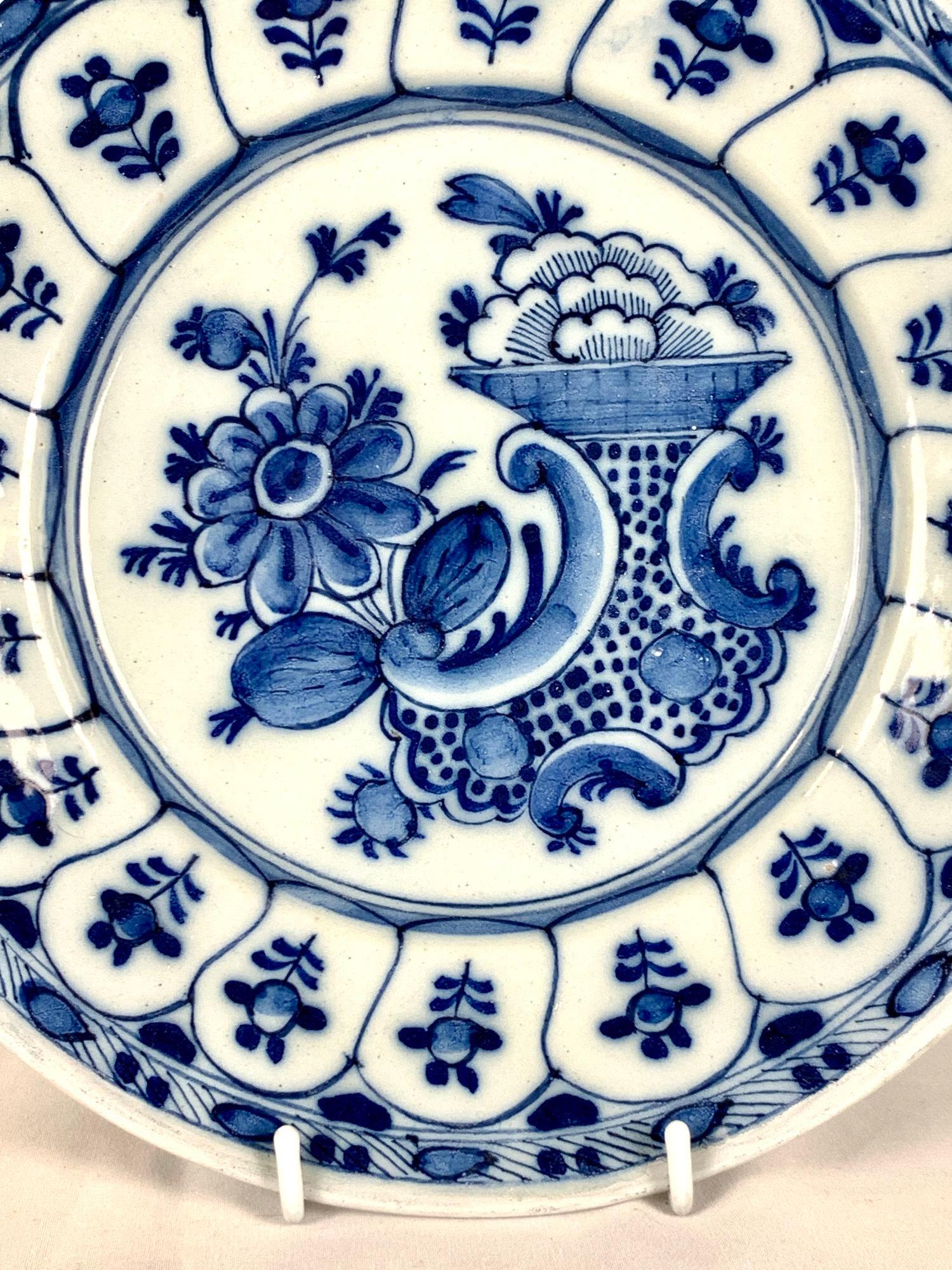 This 18th century blue and white Delft plate was hand painted circa 1780.
The lively scene in the center features flowers, flower buds, and a polka-dotted vase.
The border is decorated with 17 ogival panels, each showing a single flower.
Along the