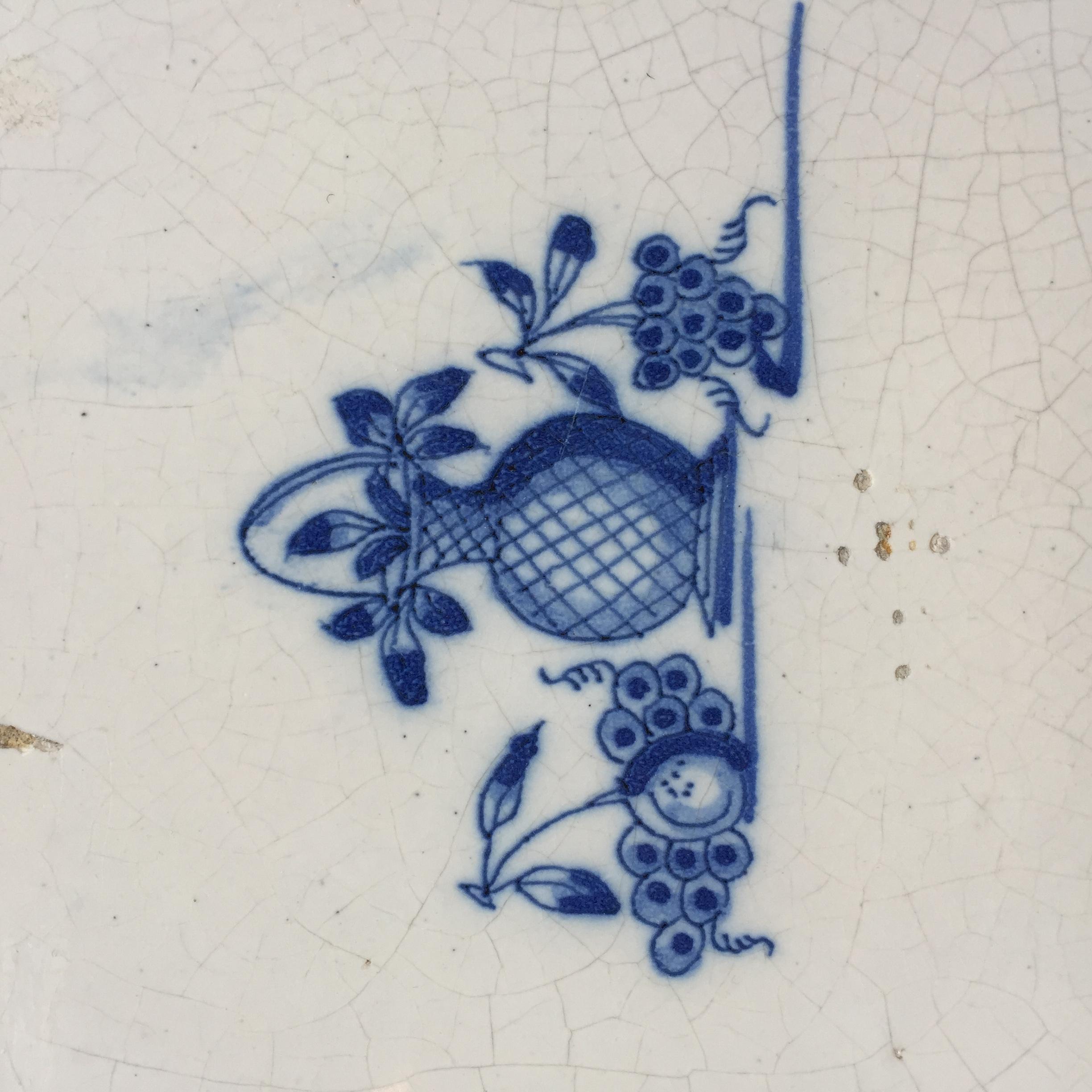 The Netherlands
Circa 1700

A fine blue and white Dutch tile with a still life painting of a vase with leaves and grapes and an apple on the sides.

The scene is painted without corner decoration to keep the focus completely on the still life