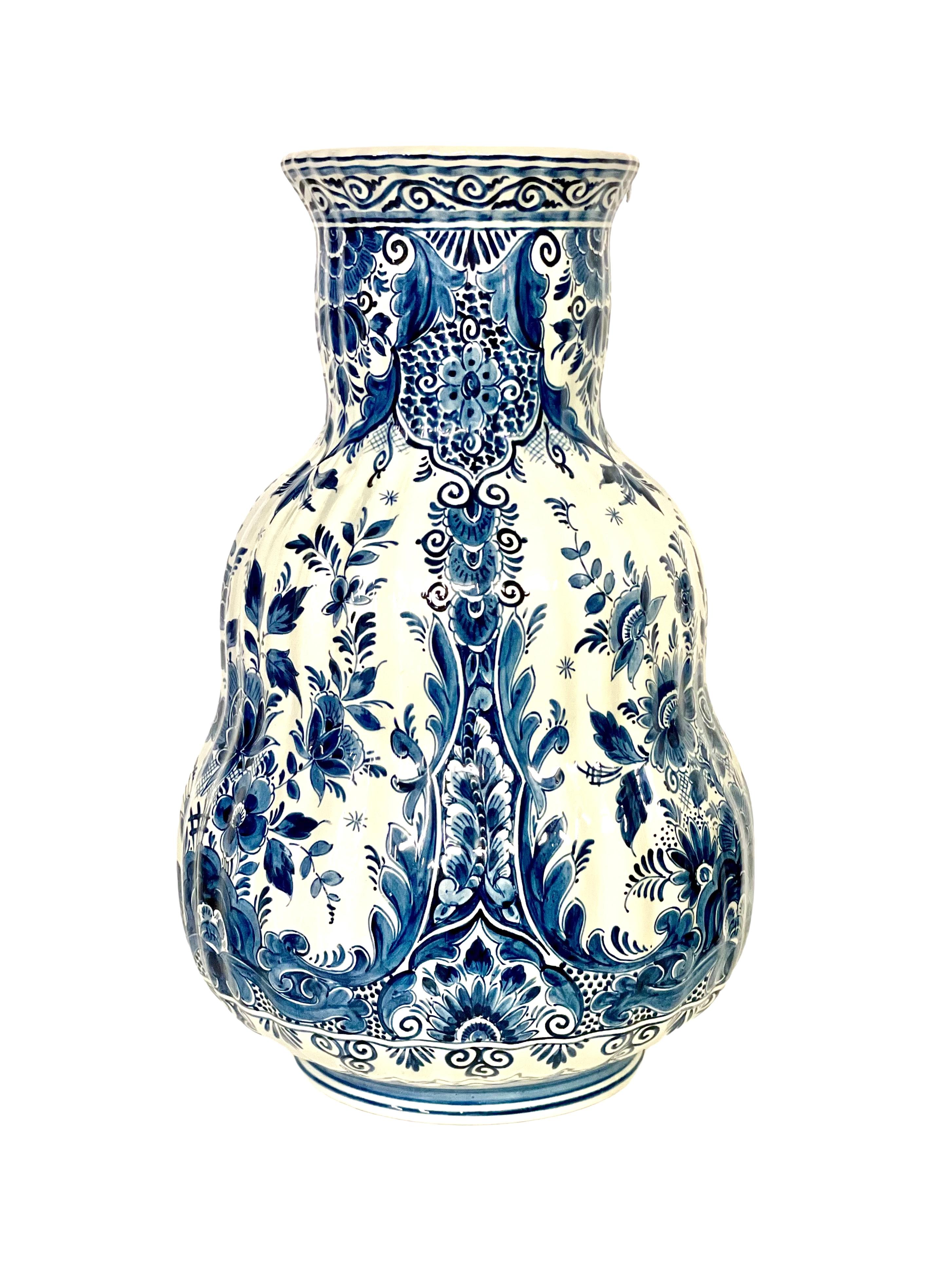 An exquisite Dutch Delft earthenware vase, hand-painted in a classic cobalt blue and white Chinoiserie design of scrolls, flowers and exuberant foliage. Tall in height, this statuesque vase has a curvaceous ribbed and pear-shaped body, which tapers