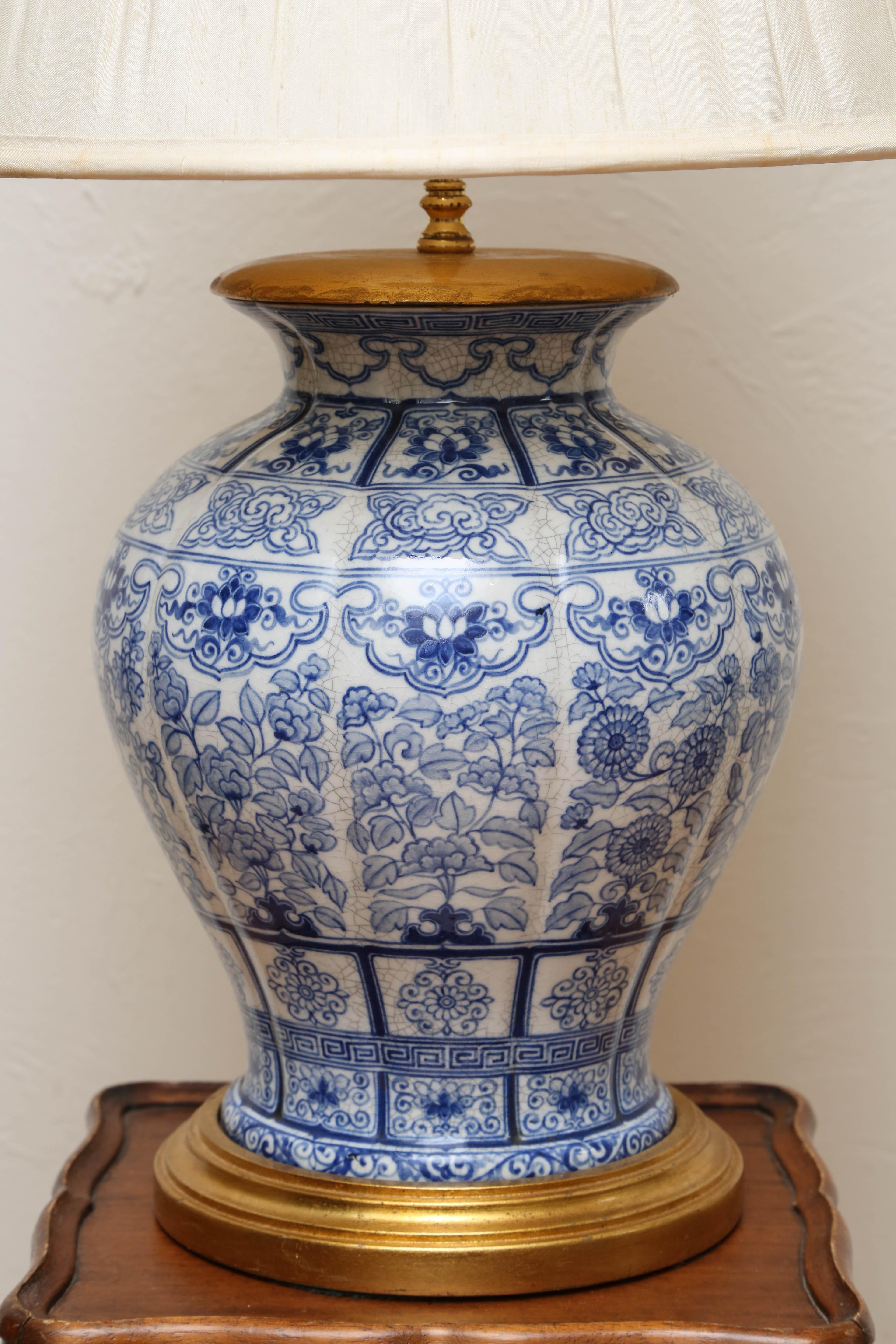 Blue and white ginger jar mounted as lamp with gilded wood base and cap. Topped with an off-white silk shade.